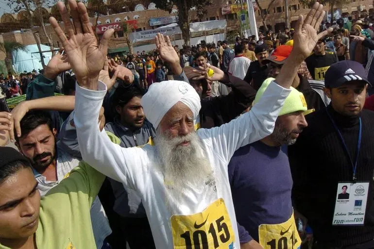 عدّاء المسافات الطويلة فوغا سينغ، المعروف بـ "تورنادو المعمم"، يرفع يديه في سباق، محاطًا بجمهور كبير، مع رقم 1015 على صدره.