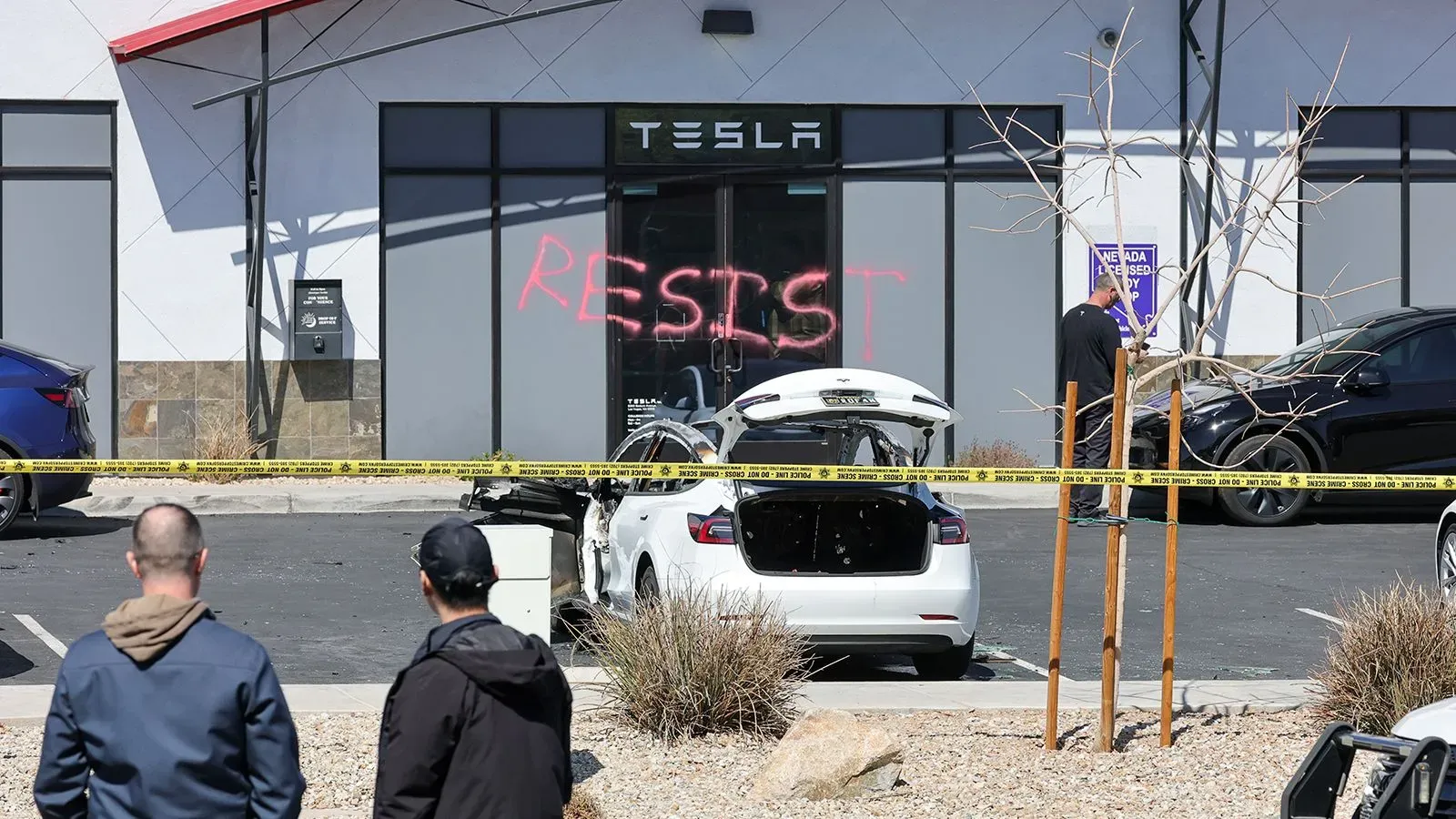 تظهر الصورة واجهة صالة عرض تسلا، حيث كُتبت كلمة "مقاومة" بالطلاء الأحمر، مع وجود سيارات متضررة وأفراد يتفقدون المكان.