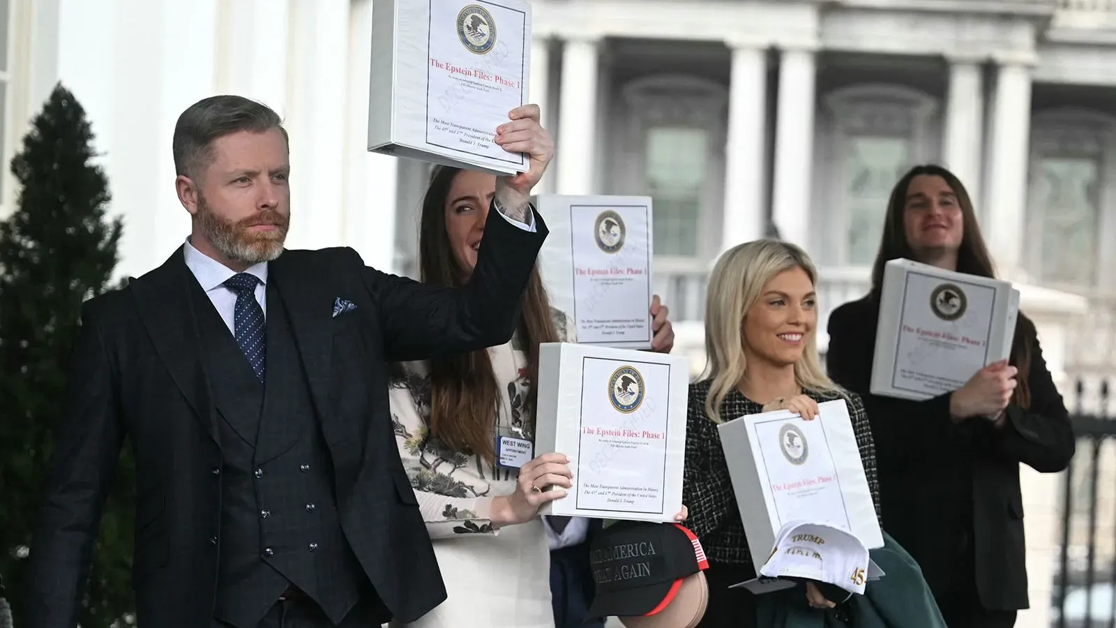 مجموعة من الأشخاص يحملون ملفات تتعلق بقضية جيفري إبشتاين أمام البيت الأبيض، مع التركيز على أهمية الشفافية في التحقيقات.