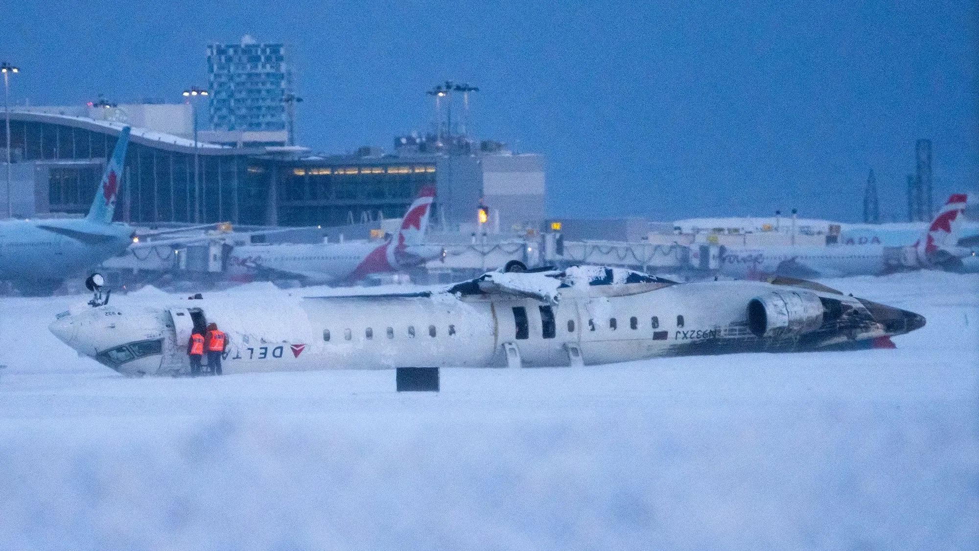 تحطم طائرة دلتا في مطار تورنتو وسط الثلوج، مع وجود رجال الإنقاذ بالقرب منها، مما يعكس مخاوف السلامة في السفر الجوي.