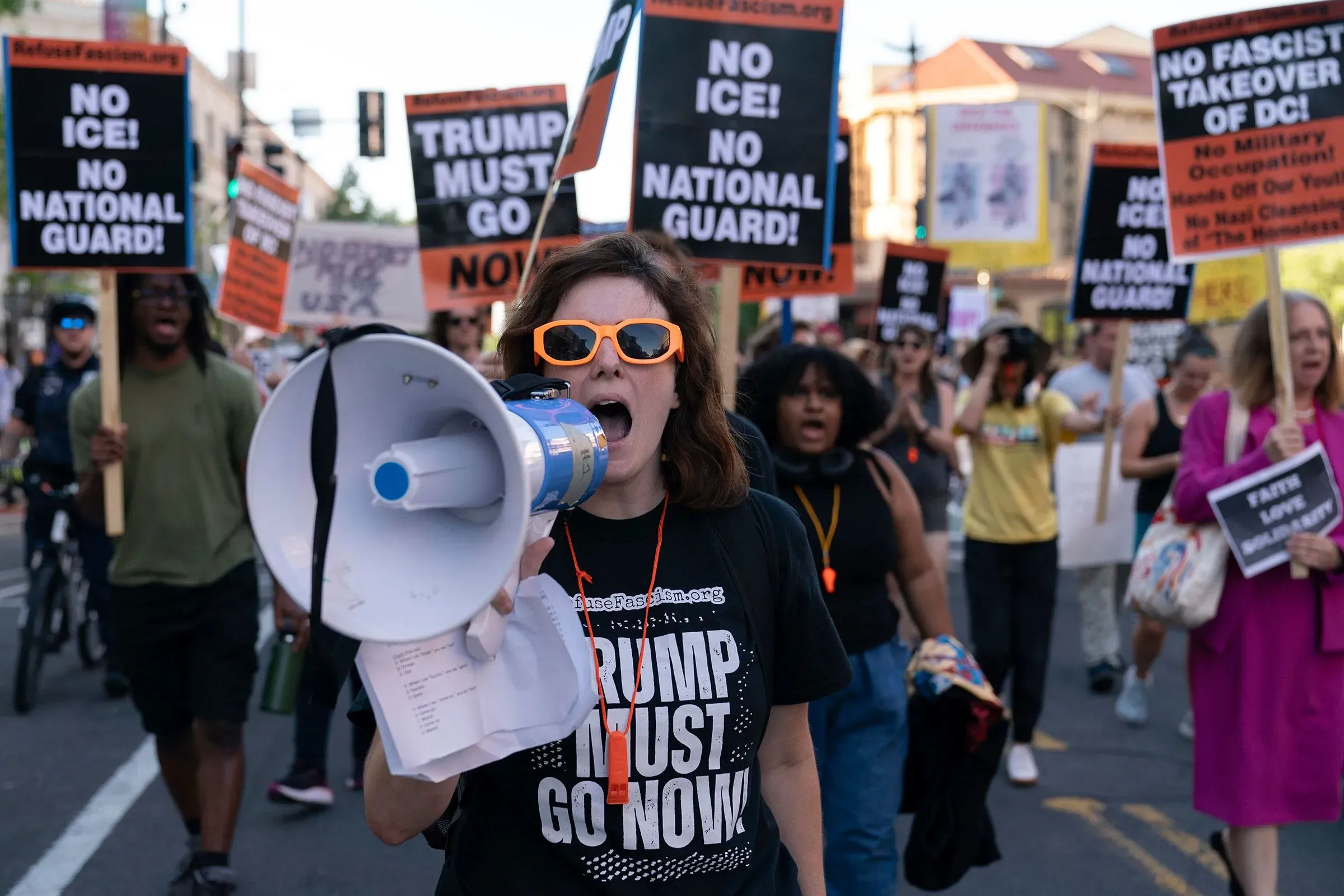 محتجون يحملون لافتات في شوارع واشنطن العاصمة، يعبرون عن معارضتهم لسياسات الهجرة وإجراءات إدارة ترامب، بينما تتصدر امرأة ترتدي نظارات شمسية.