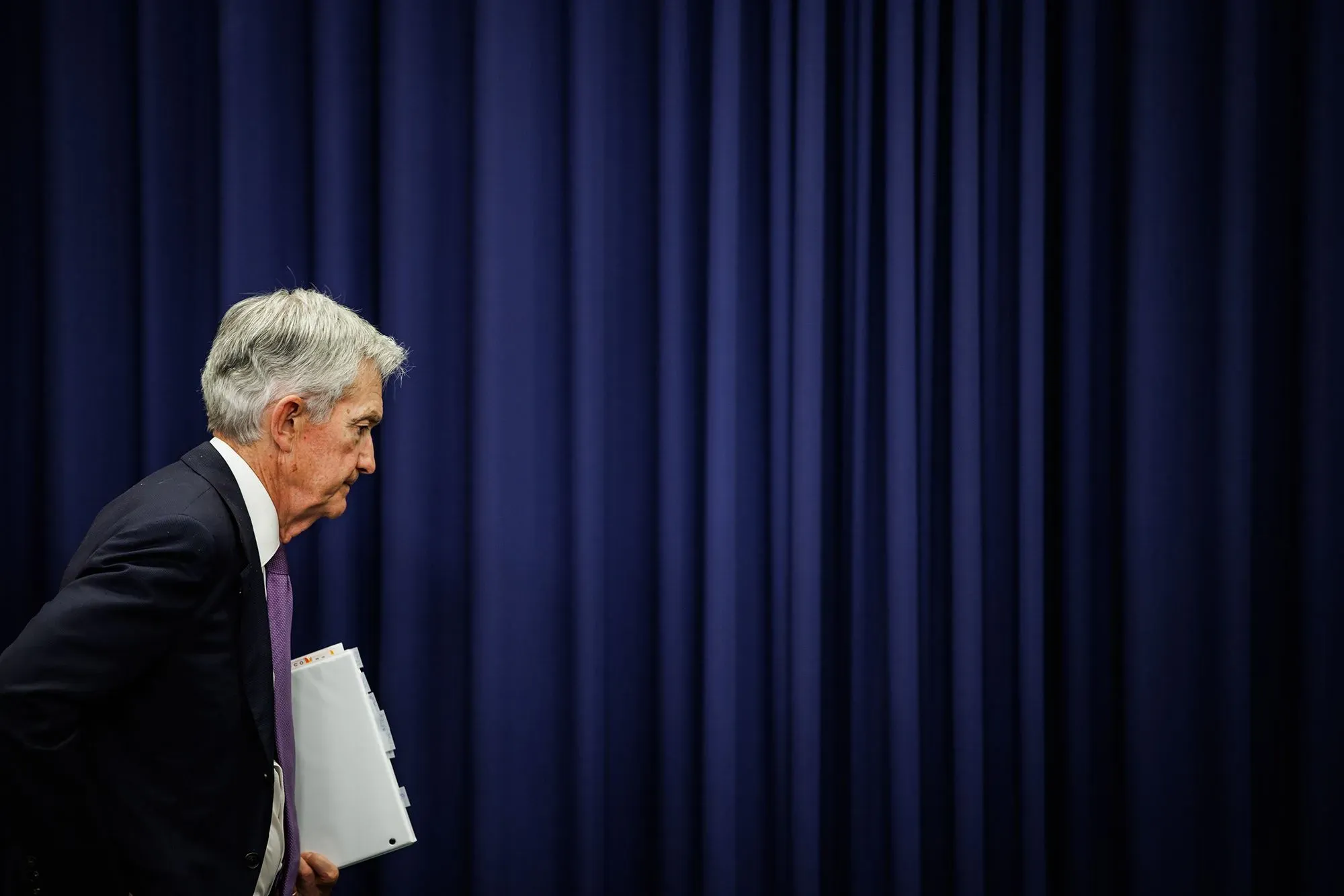 جيروم باول، رئيس الاحتياطي الفيدرالي، يغادر قاعة المؤتمر بعد الإعلان عن تخفيض أسعار الفائدة، مع خلفية زرقاء.