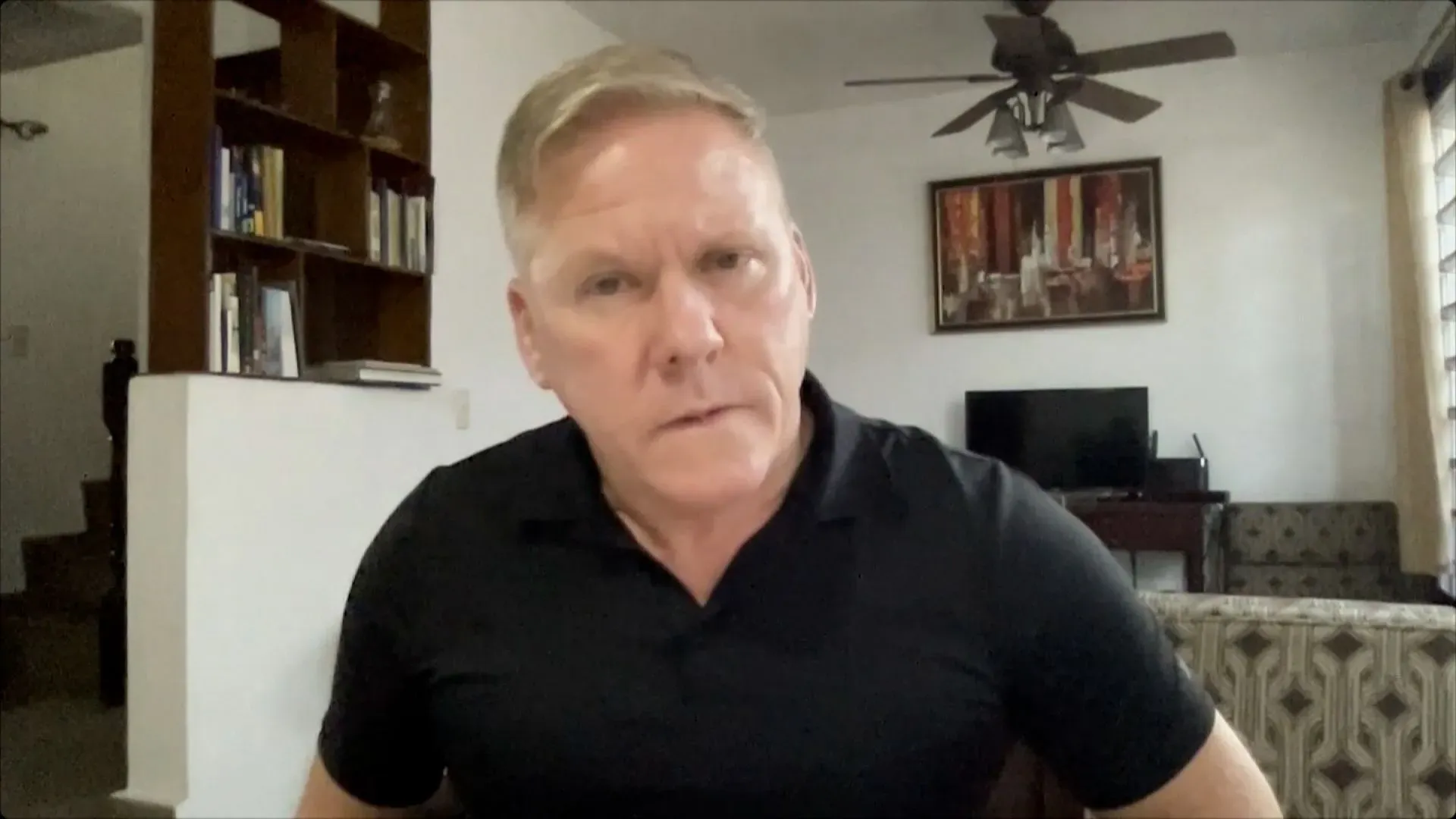 رجل يجلس في غرفة معيشة، يبدو عليه التركيز والجدية، مع خلفية تحتوي على أرفف كتب وأثاث مريح، في سياق نقاش حول قضايا قانونية وسياسية.