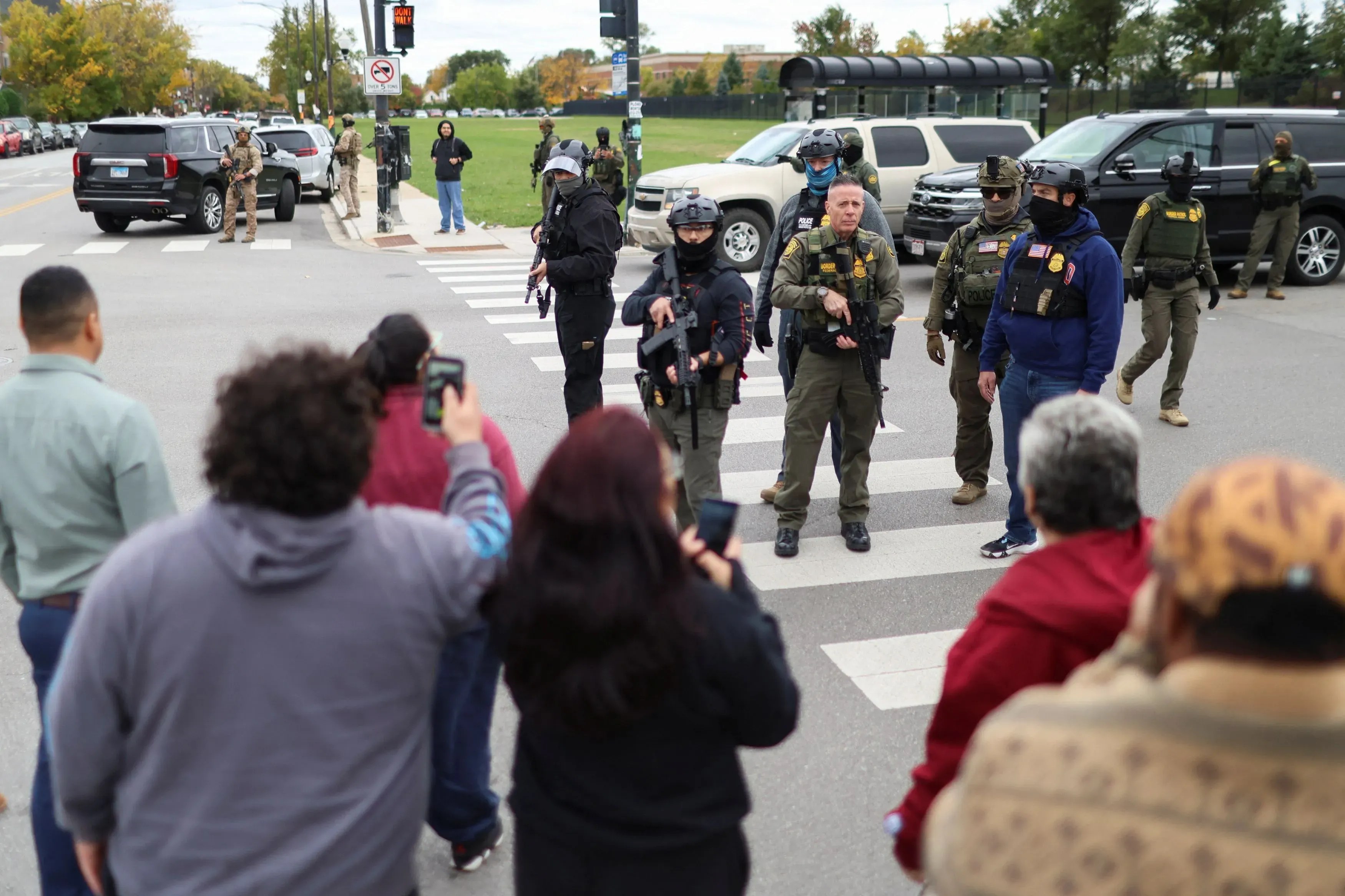 مجموعة من الأشخاص يراقبون عملاء الهجرة والجمارك في مينيابوليس، بينما يرتدي بعضهم ملابس عسكرية. يظهر المتطوعون يتوثقون من الاعتقالات.