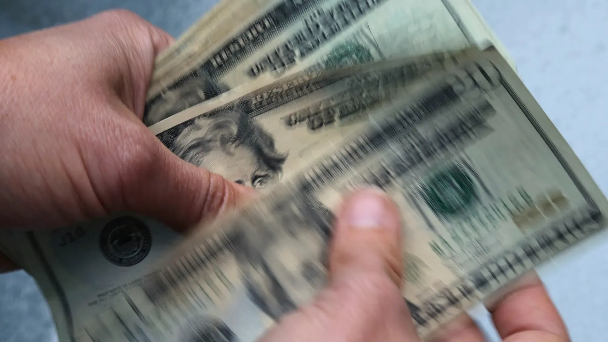 يد تُمسك بعدة أوراق نقدية من فئة عشرين دولارًا، مما يعكس مشهدًا يتعلق بالعجز الفيدرالي والضغوط المالية في الكونغرس.