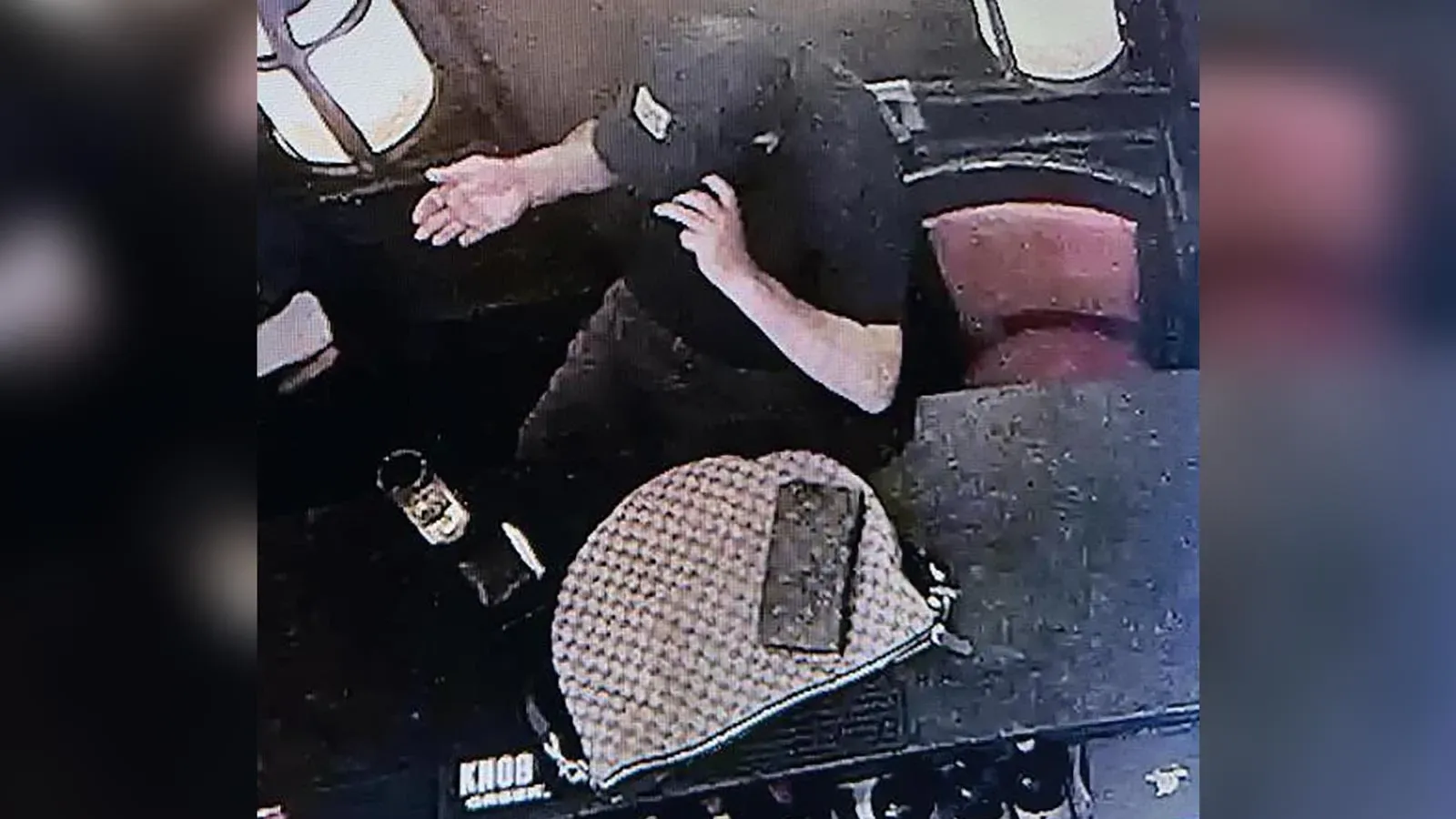 رجل يجلس في مطعم، يده مرفوعة، بينما توجد حقيبة بالقرب منه. الصورة توثق لحظة قبل سرقة حقيبة وزيرة الأمن الداخلي.