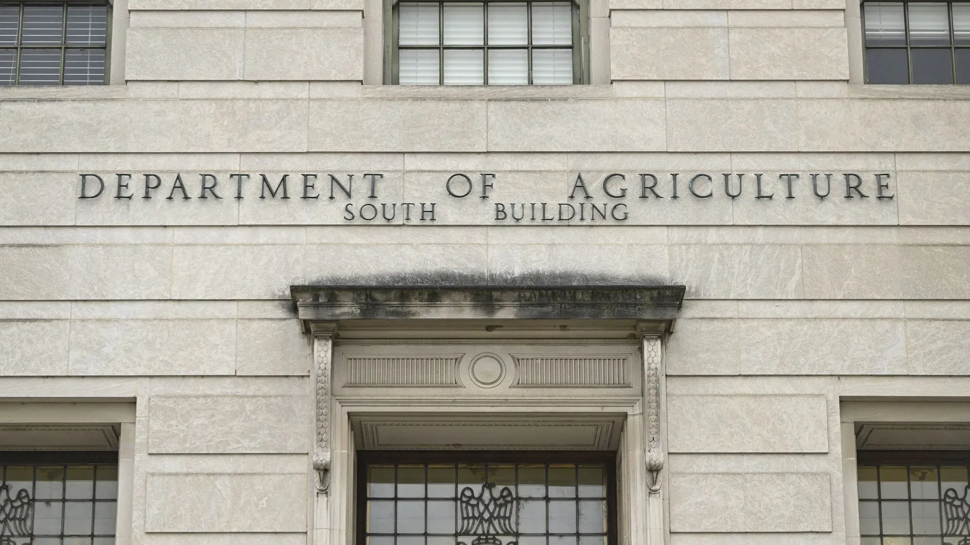 واجهة مبنى وزارة الزراعة الأمريكية، مع لافتة توضح الاسم وتفاصيل المبنى، تشير إلى قضايا تتعلق بوظائف الموظفين الفيدراليين.