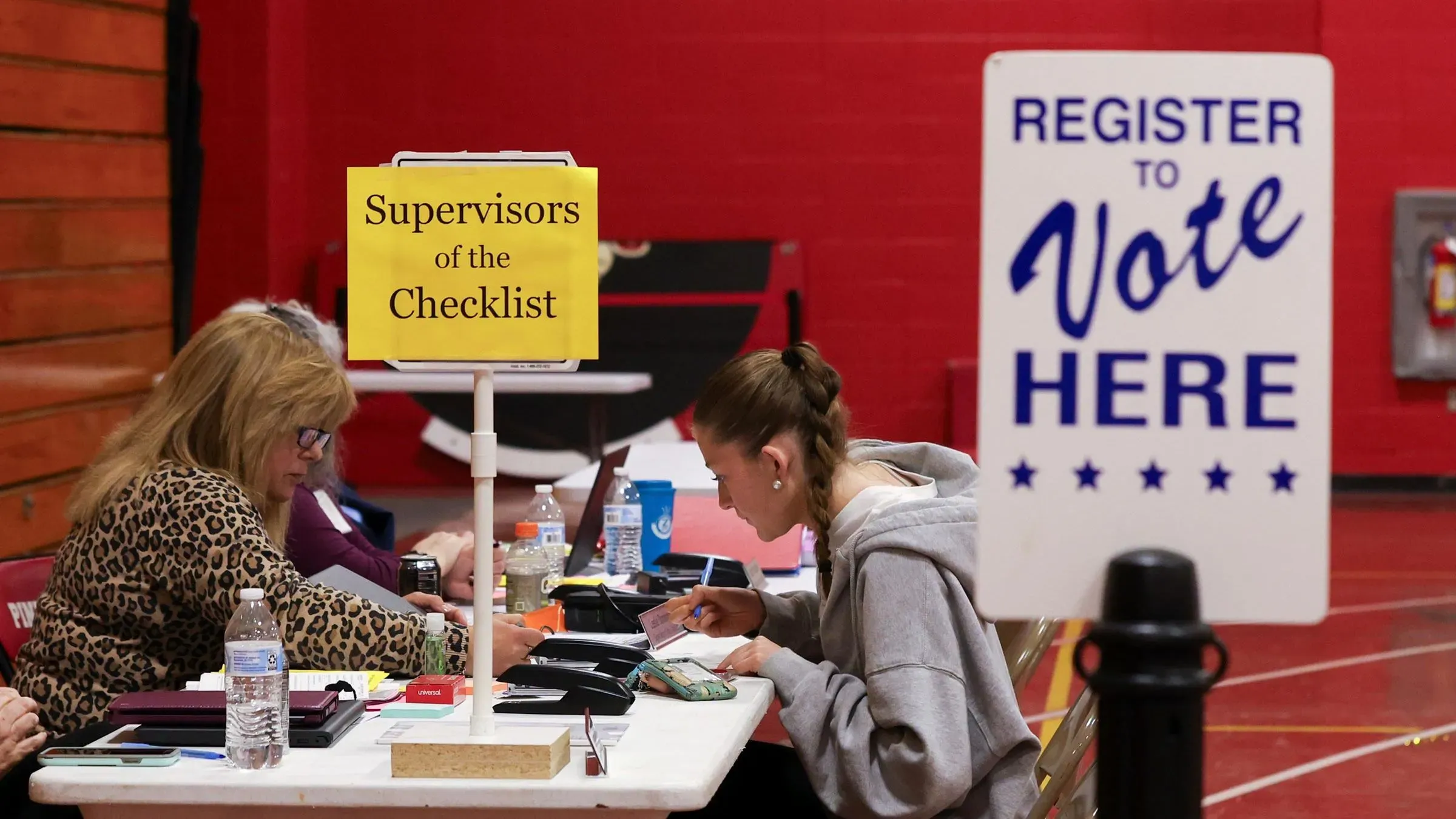 سيدة تسجل للتصويت في مركز انتخابي، مع لافتة تشير إلى مشرفي القائمة، تعكس جهود التسجيل في الانتخابات الأمريكية.