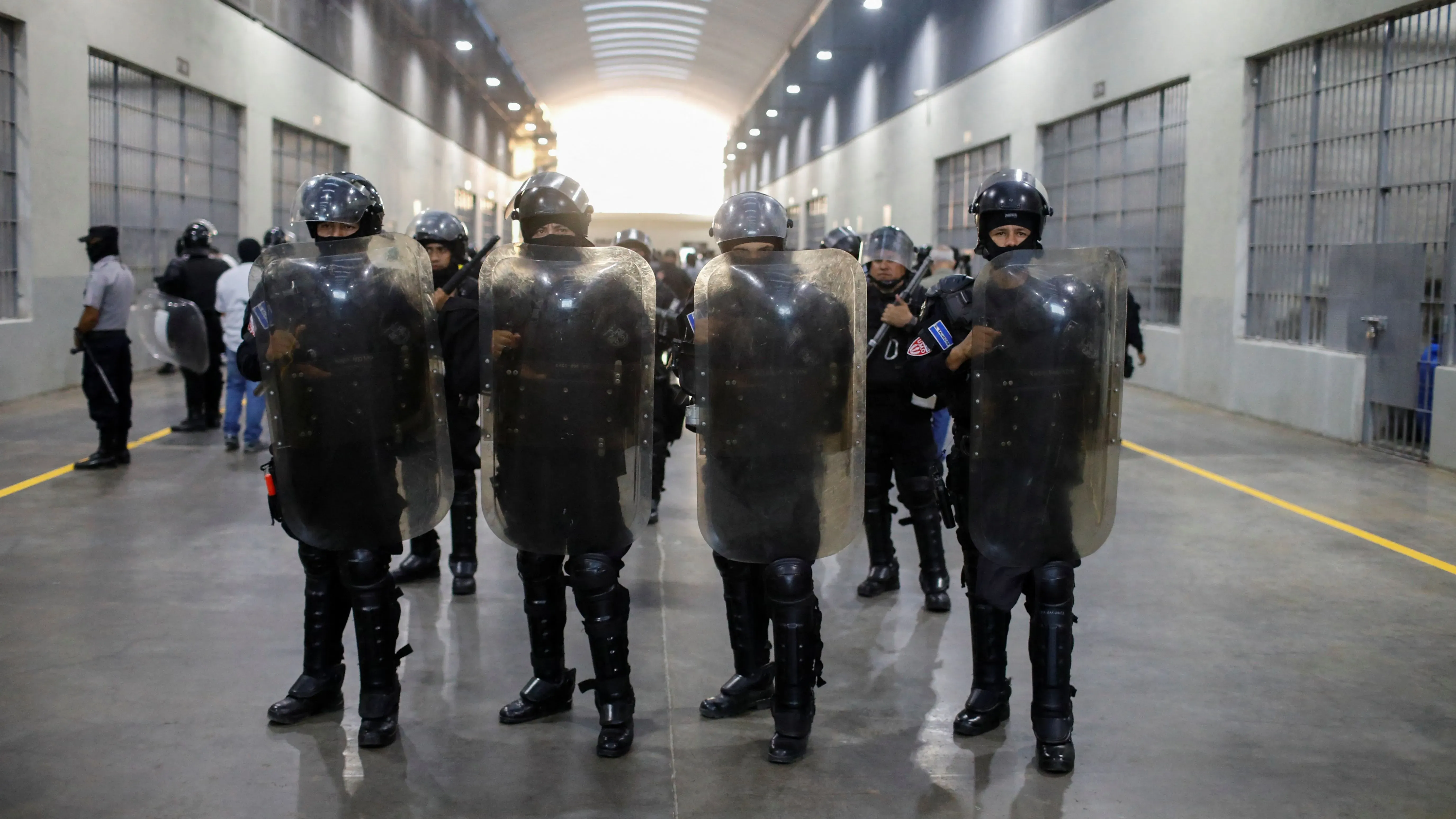 قوات أمنية ترتدي دروعًا واقية في ممر سجن كبير بالسلفادور، خلال جلسة استماع قانونية حول ترحيل المهاجرين.