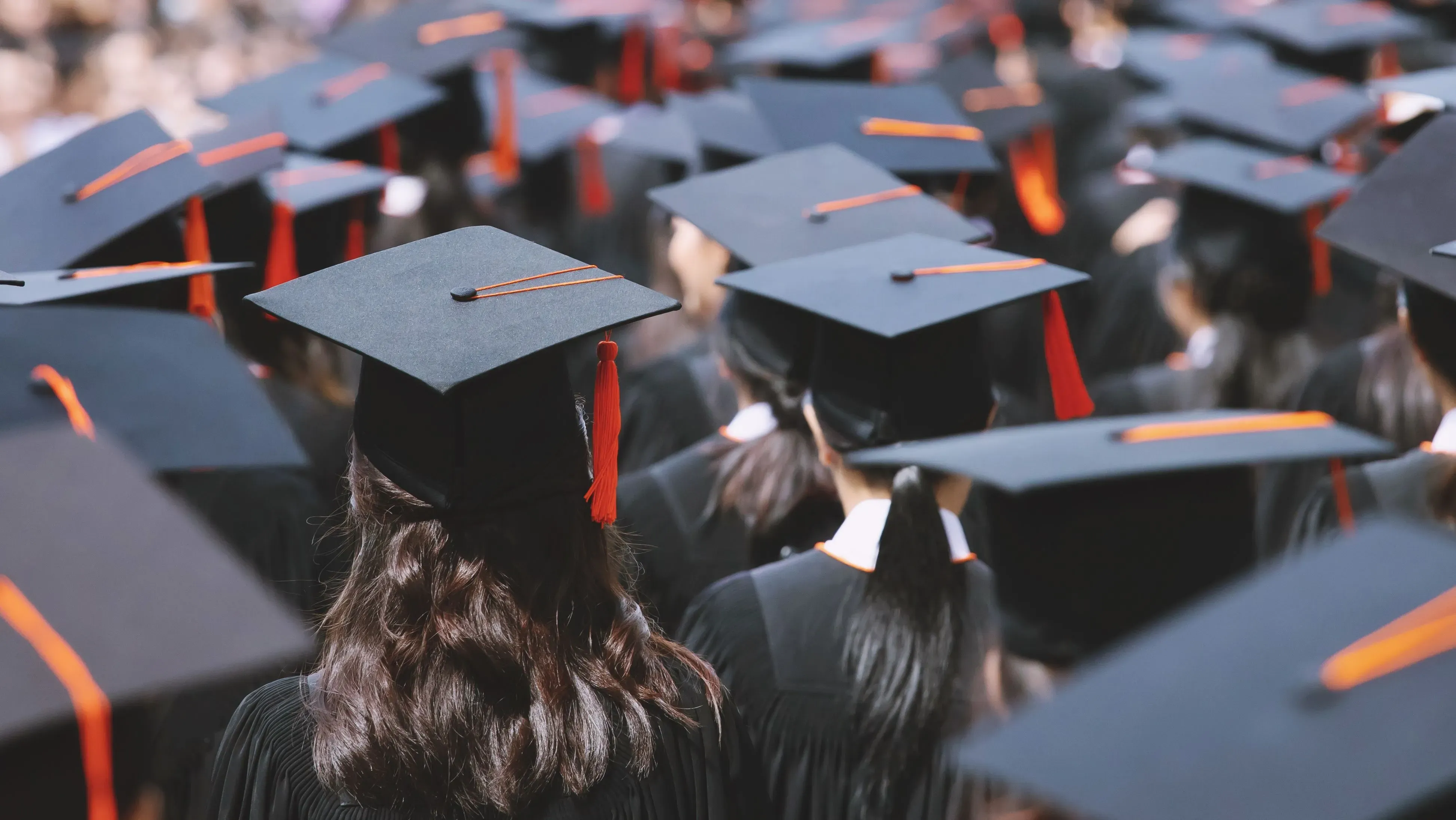حفل تخرج يضم مجموعة من الطلاب يرتدون قبعات التخرج والعباءات، مع التركيز على تفاصيل القبعات المميزة بشريط برتقالي.