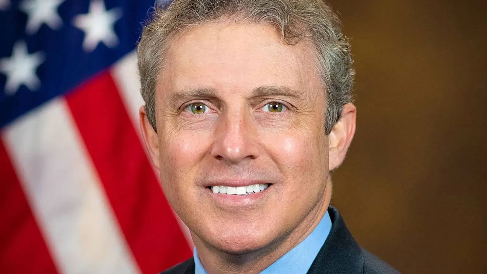 صورة للمستشار الخاص هامبتون ديلينجر، مبتسم، مع العلم الأمريكي في الخلفية، بعد إعلان تنازله عن الدعوى القضائية ضد إقالته من قبل ترامب.