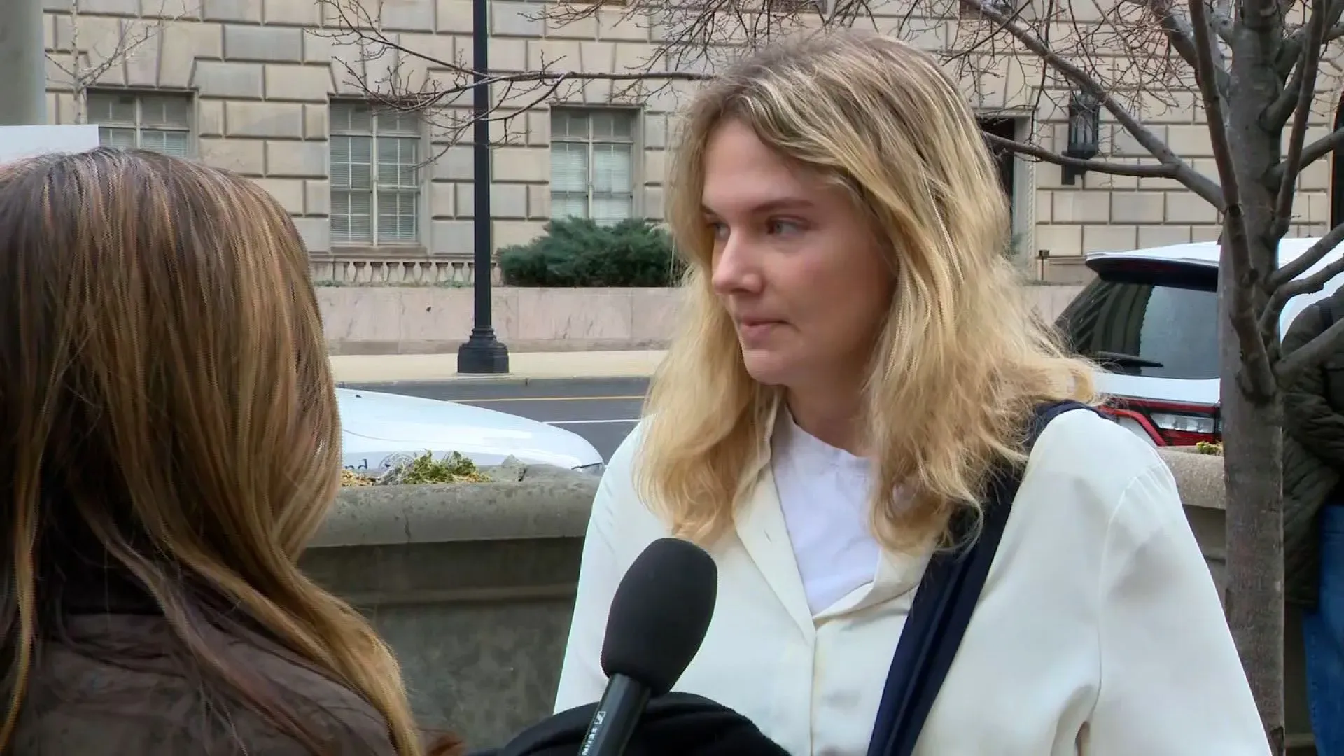 موظفة فيدرالية تتحدث مع صحفية خارج مكتب حكومي، تعبر عن قلقها بشأن التسريحات الحكومية الجماعية وتأثيرها على الوظائف.