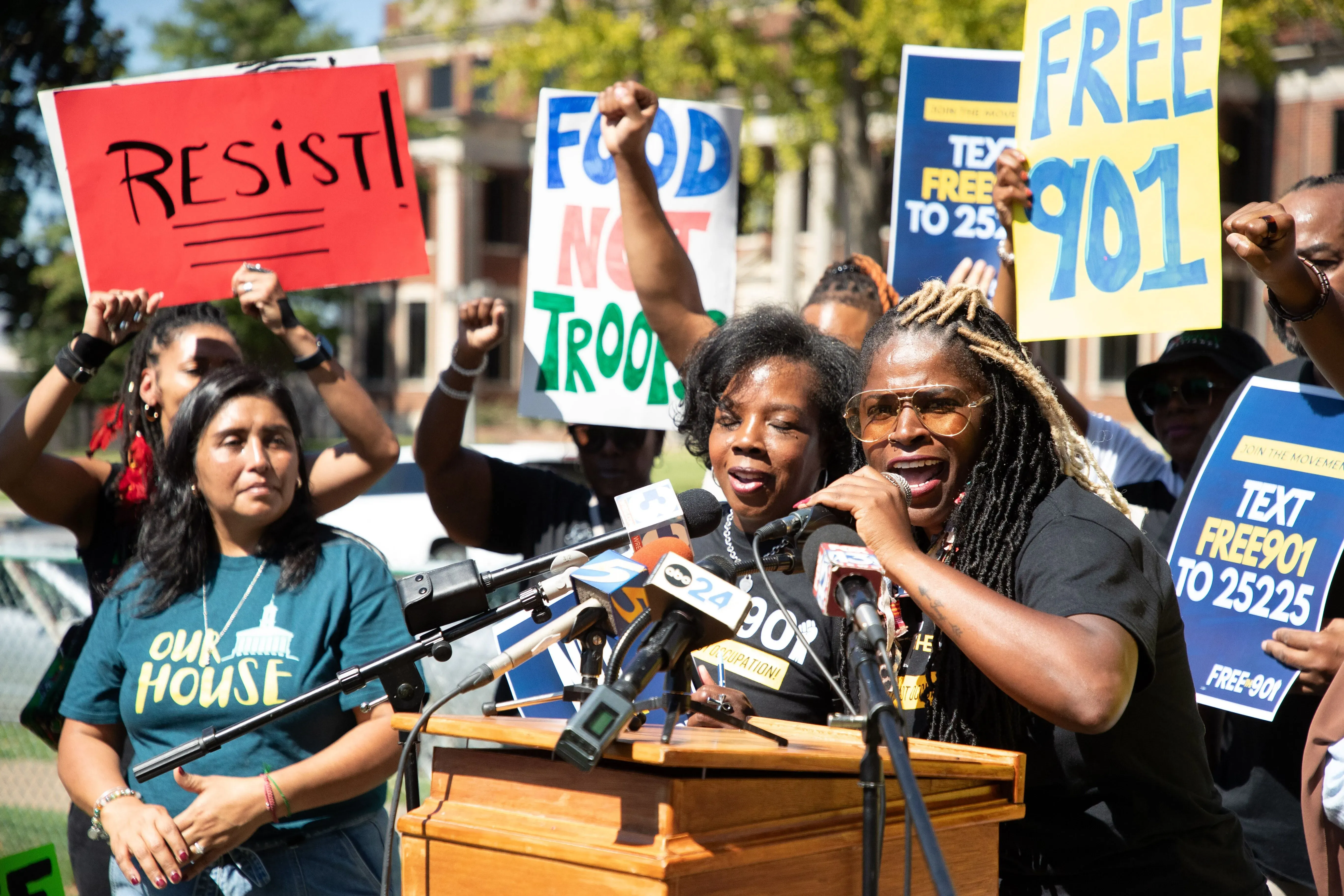 محتجون في ممفيس يتحدثون خلال فعالية، حاملين لافتات تطالب بإلغاء إرسال القوات الفيدرالية، مع وجود منصة إعلامية في المقدمة.