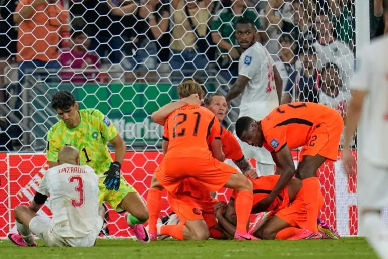 لاعبو منتخب هولندا يحتفلون بهدف في مرمى المغرب خلال مباراة كأس العالم، مع حارس المغرب وجمهور في الخلفية.