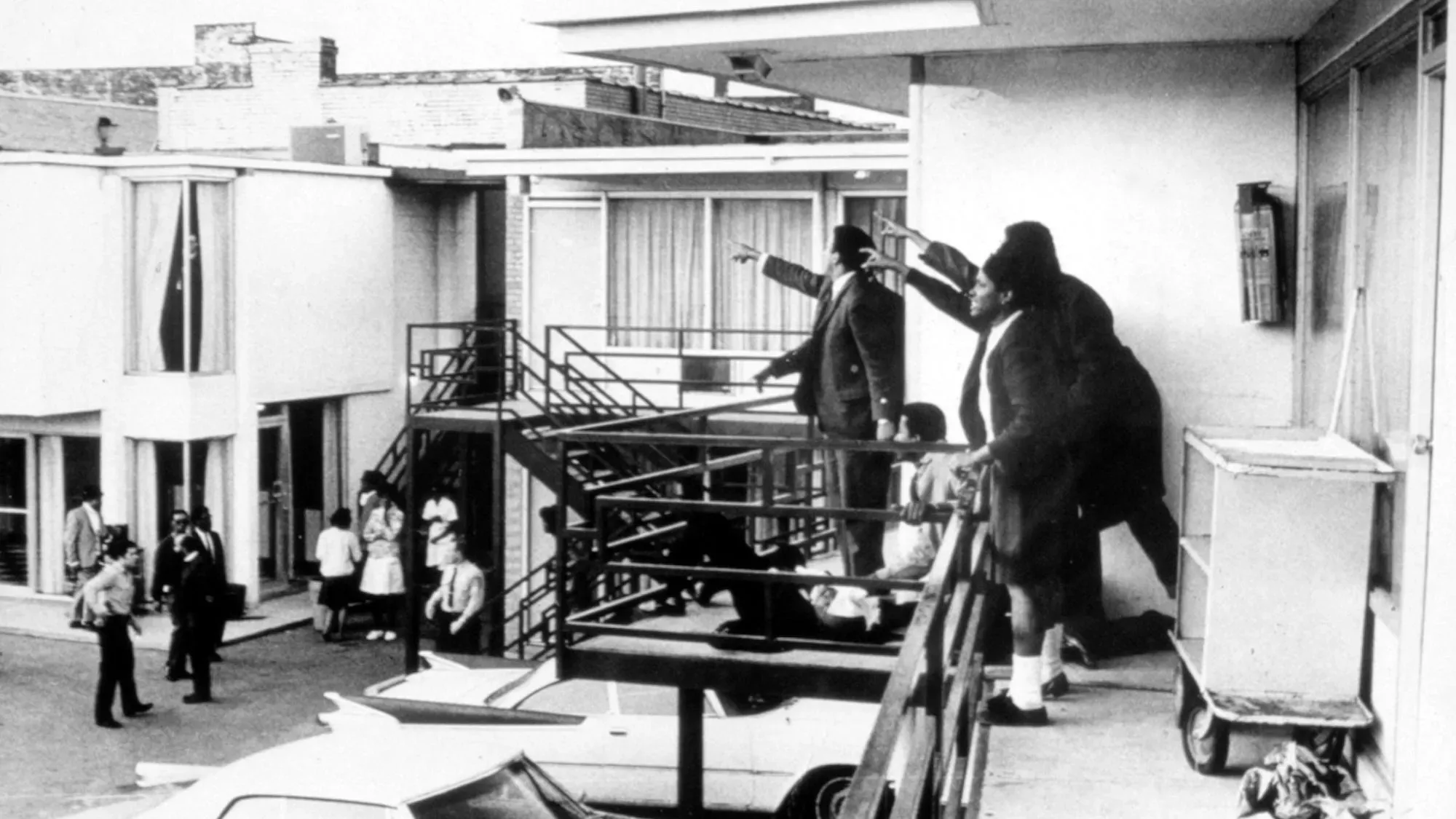 صورتي مجموعة من الأشخاص يتجمعون على شرفة في فندق، مع إيماءات تشير إلى مكان وقوع حادث اغتيال مارتن لوثر كينغ، في سياق تاريخي مهم.