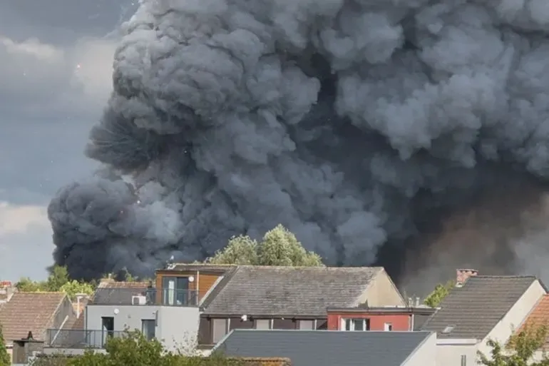 سحب كثيفة من الدخان الأسود تتصاعد فوق المنازل، نتيجة حريق هائل في المسرح الرئيسي لمهرجان تومورولاند البلجيكي.