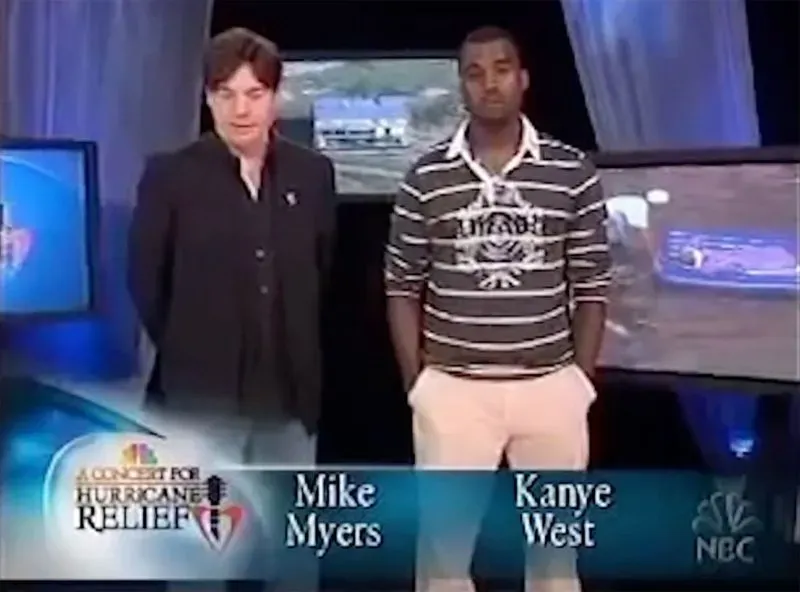 كanye ويست ومايك مايرز في برنامج خاص لجمع التبرعات بعد إعصار كاترينا، يتحدثان أمام شاشات تُظهر آثار الدمار.