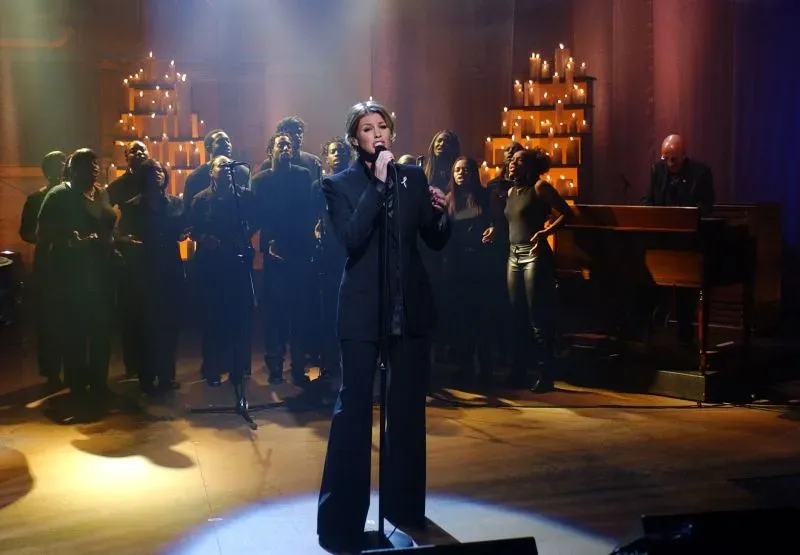 مغنية تؤدي على المسرح محاطًة بجوقة في حدث خيري، مع إضاءة دافئة وشموع خلفية، لدعم المتضررين من الكوارث.