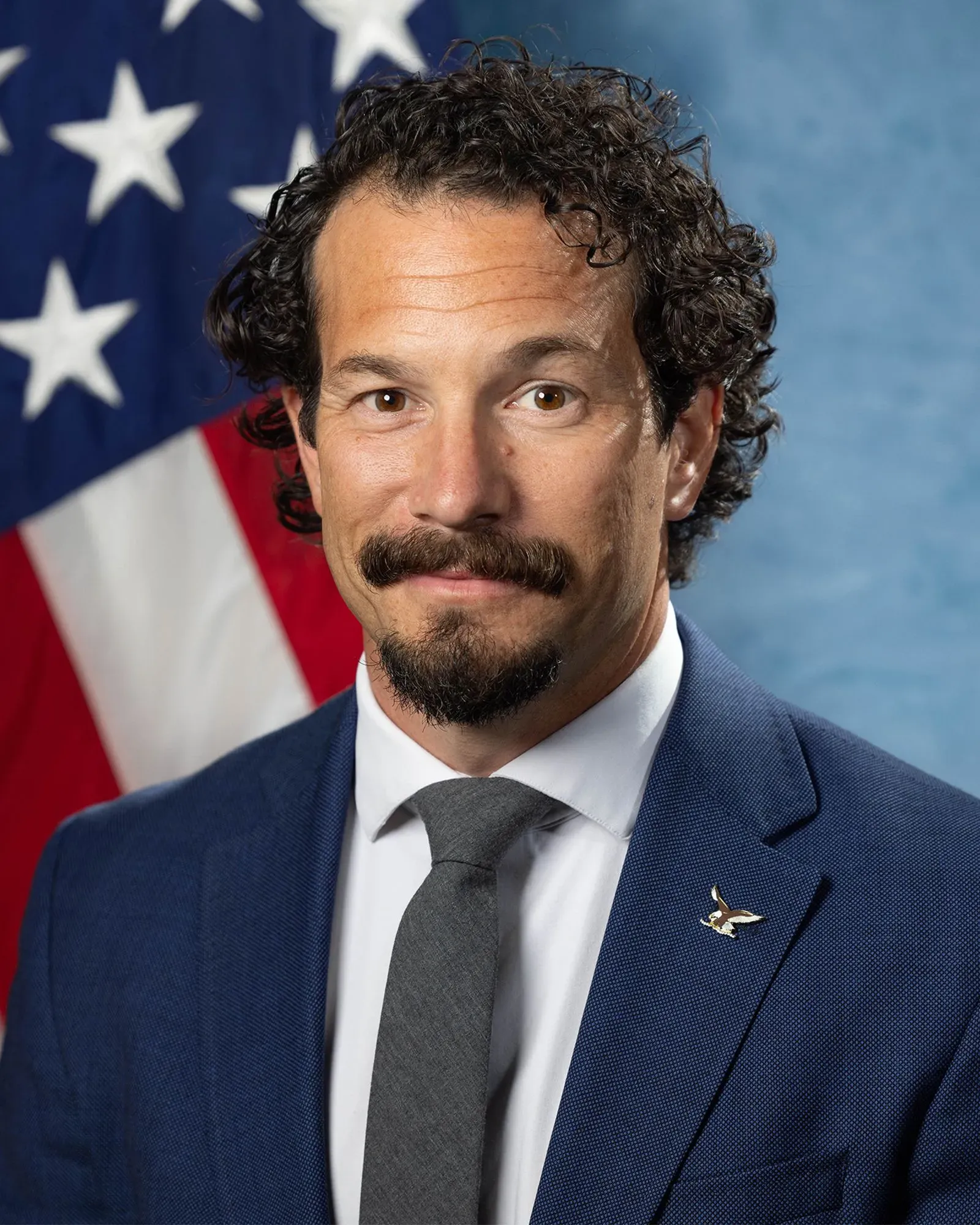 صورة لرجل يرتدي بدلة رسمية مع ربطة عنق، يقف أمام علم أمريكي، ويبدو أنه أحد كبار مسؤولي مكتب التحقيقات الفيدرالي السابقين.