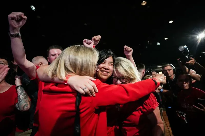 احتفال مجموعة من الأشخاص يرتدون ملابس حمراء بفوزهم في الانتخابات الأسترالية، مع تعبيرات فرح ونجاح في أجواء حماسية.