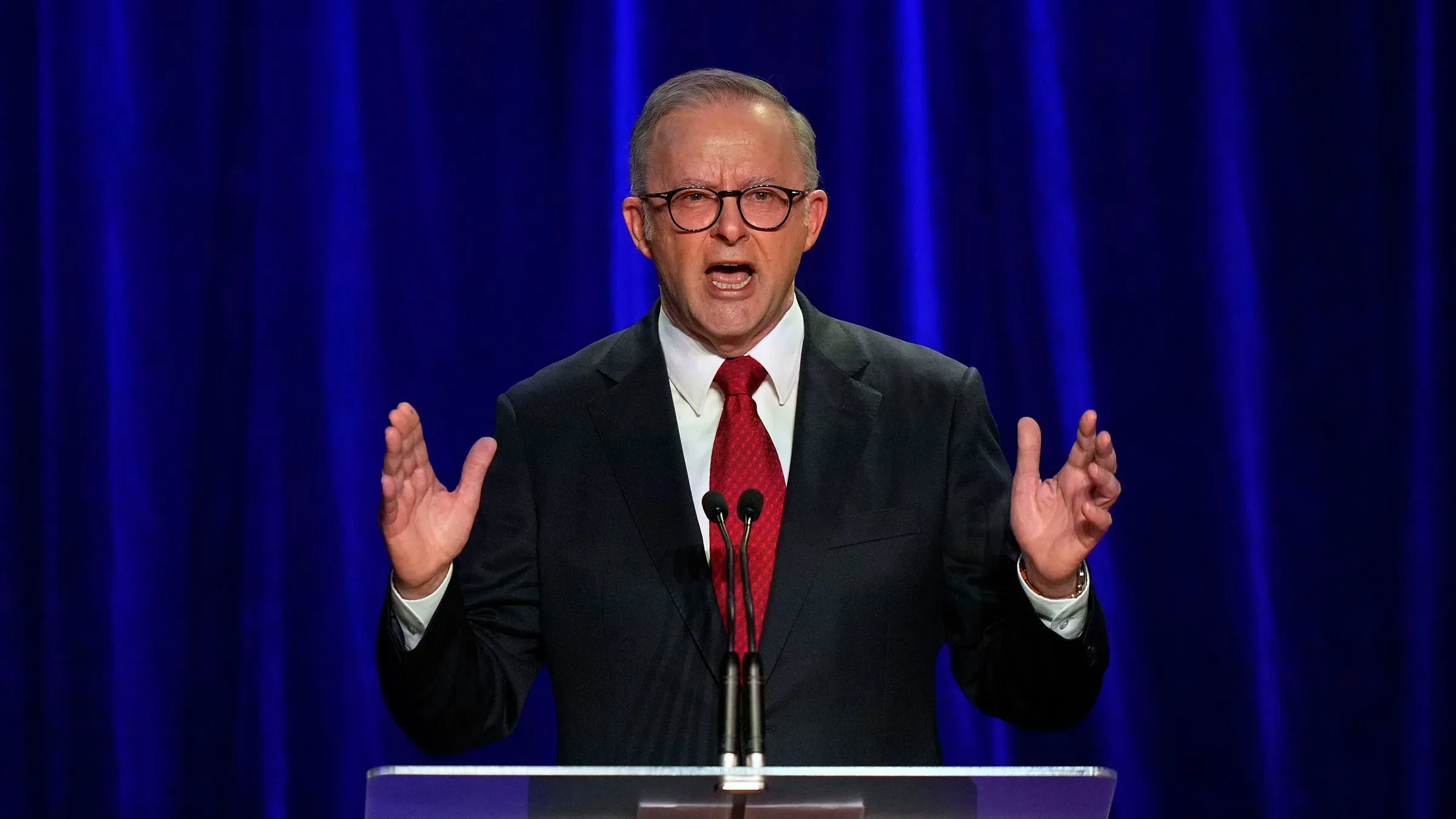 رئيس الوزراء الأسترالي أنتوني ألبانيز يتحدث بحماس خلال مؤتمر صحفي بعد فوز حزبه في الانتخابات، مع خلفية زرقاء.