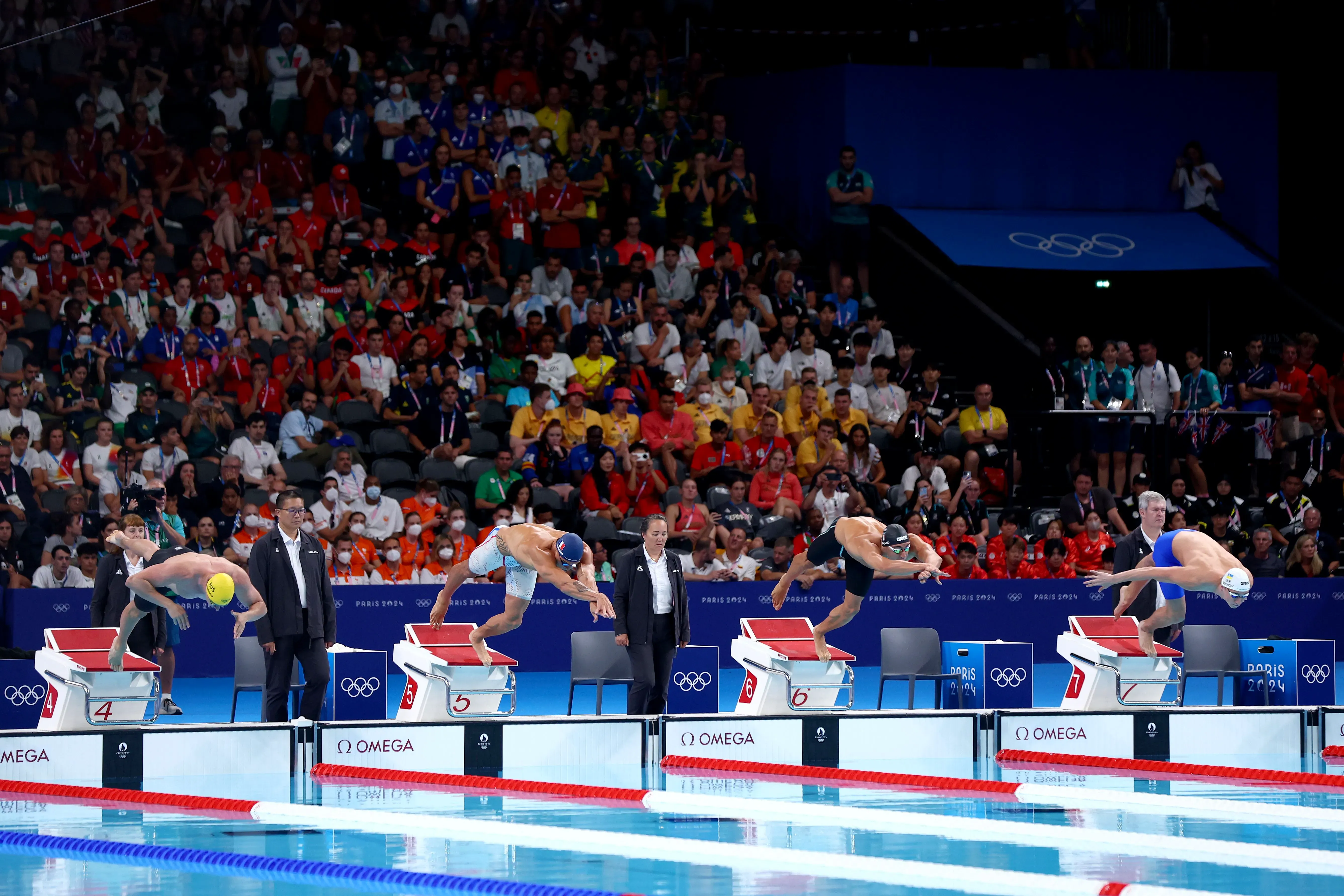 سباحون يتنافسون في سباق 50 مترًا حرة خلال بطولة العالم للألعاب المائية 2024 في الدوحة، مع جمهور واسع في الخلفية.