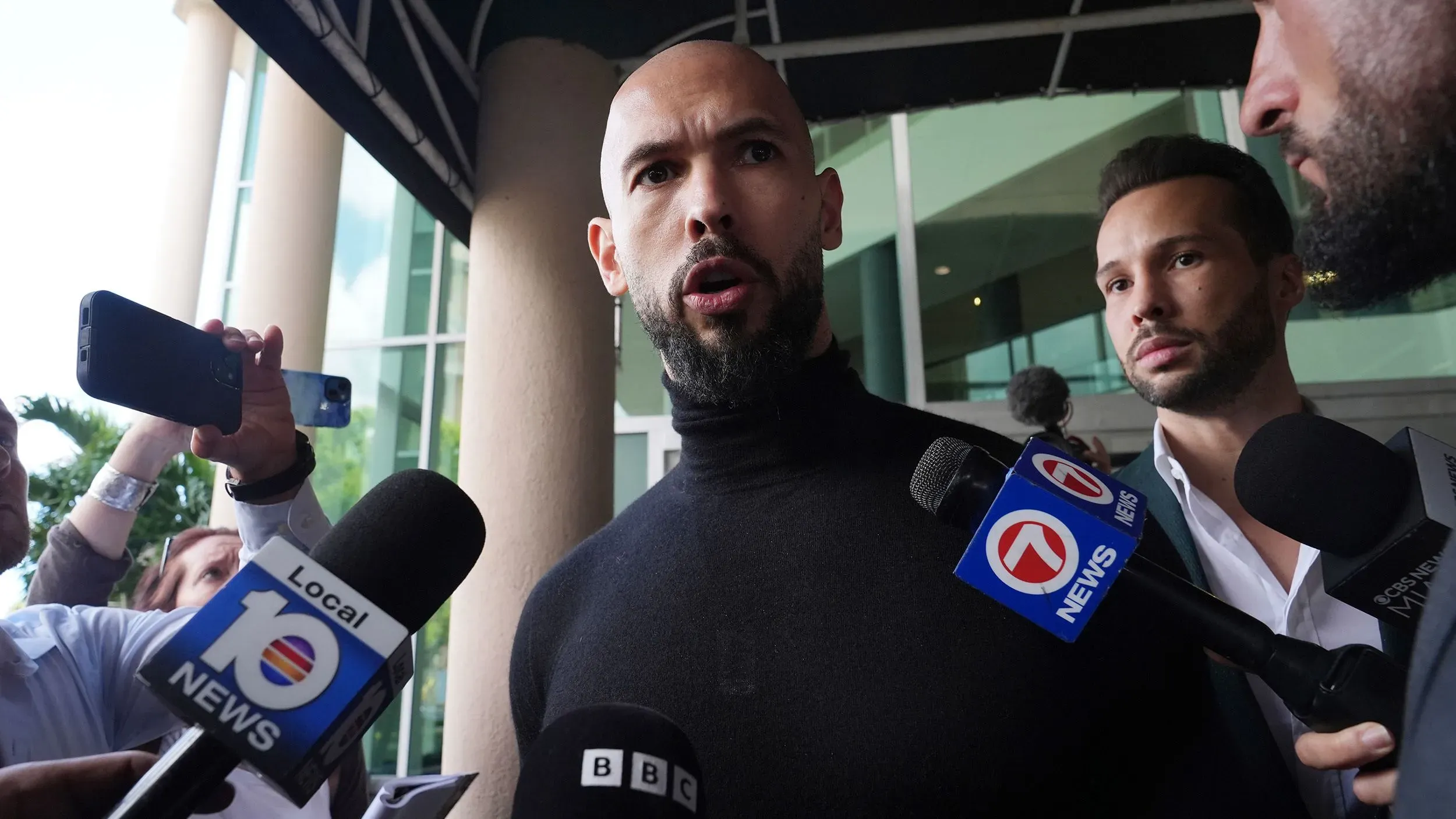 أندرو تيت يتحدث للصحفيين خارج مطار فورت لودرديل، محاطًا بعدد من المراسلين، وسط تحقيقات جنائية ضده وشقيقه.