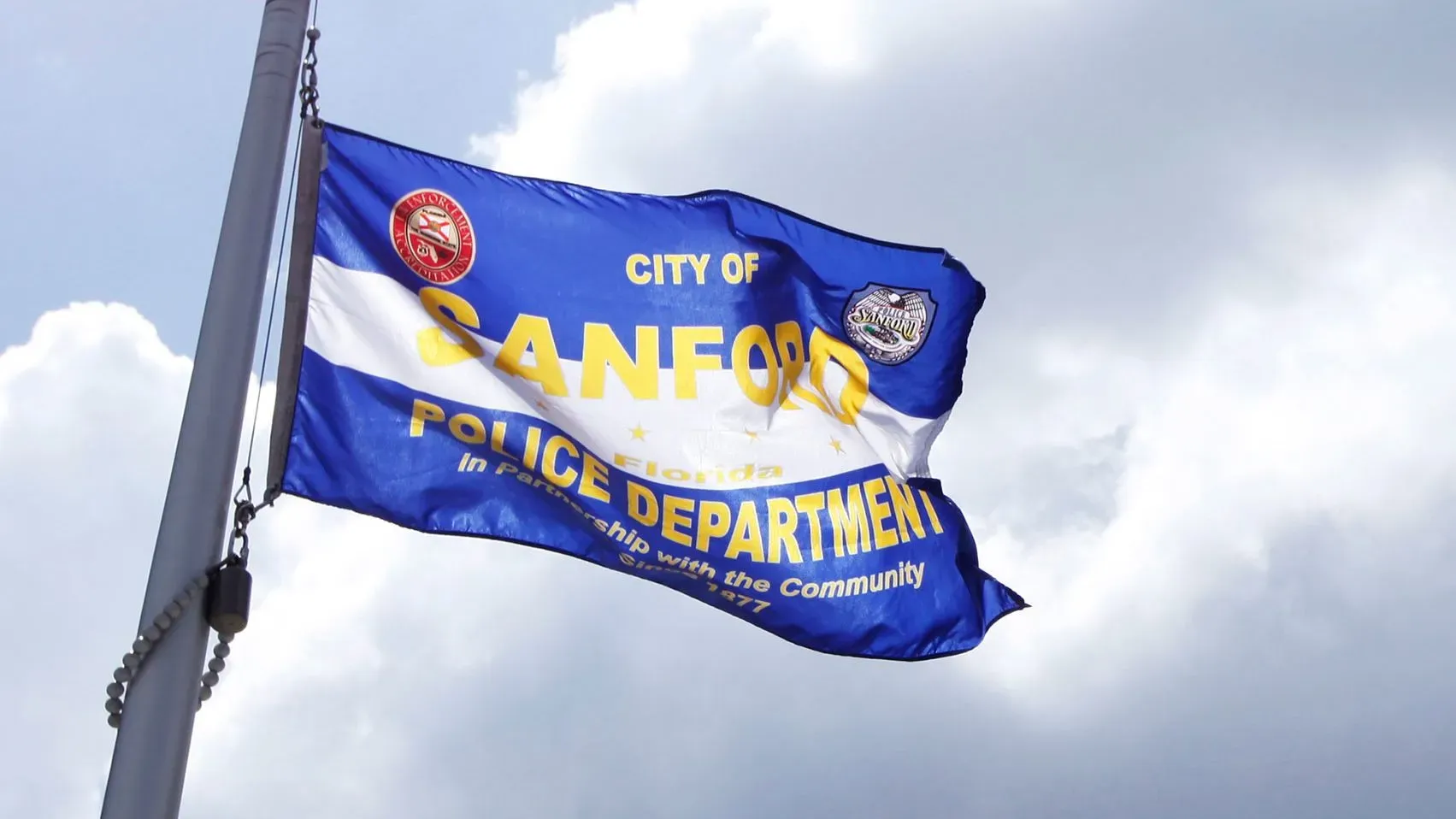 علم شرطة مدينة سانفورد يرفرف في الهواء، مع شعار الشرطة، في سياق التحقيق في تهديد إطلاق نار في مدرسة ثانوية.