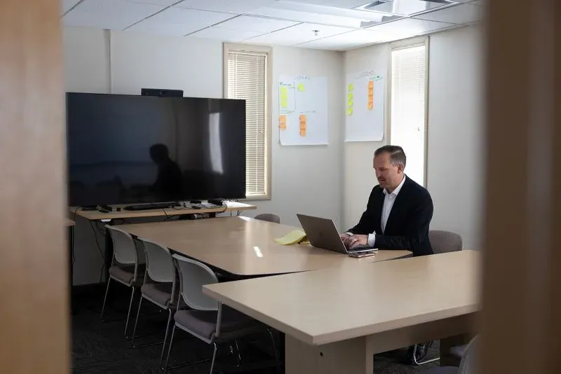 محامي يجلس أمام كمبيوتر محمول في غرفة اجتماعات، مع شاشة كبيرة وملاحظات ملصقة على الجدران، في سياق قضايا الاعتداء الجنسي ضد شون كومبس.