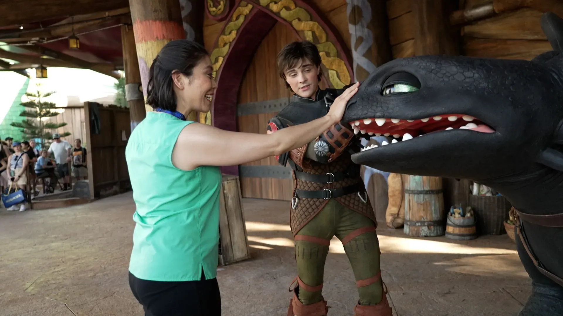 امرأة تتفاعل مع تنين مقلد في منتزه "إبيك يونيفرس" بديكور مستوحى من "كيف تدرب تنينك"، مع شخص يرتدي زي شخصية من الفيلم.