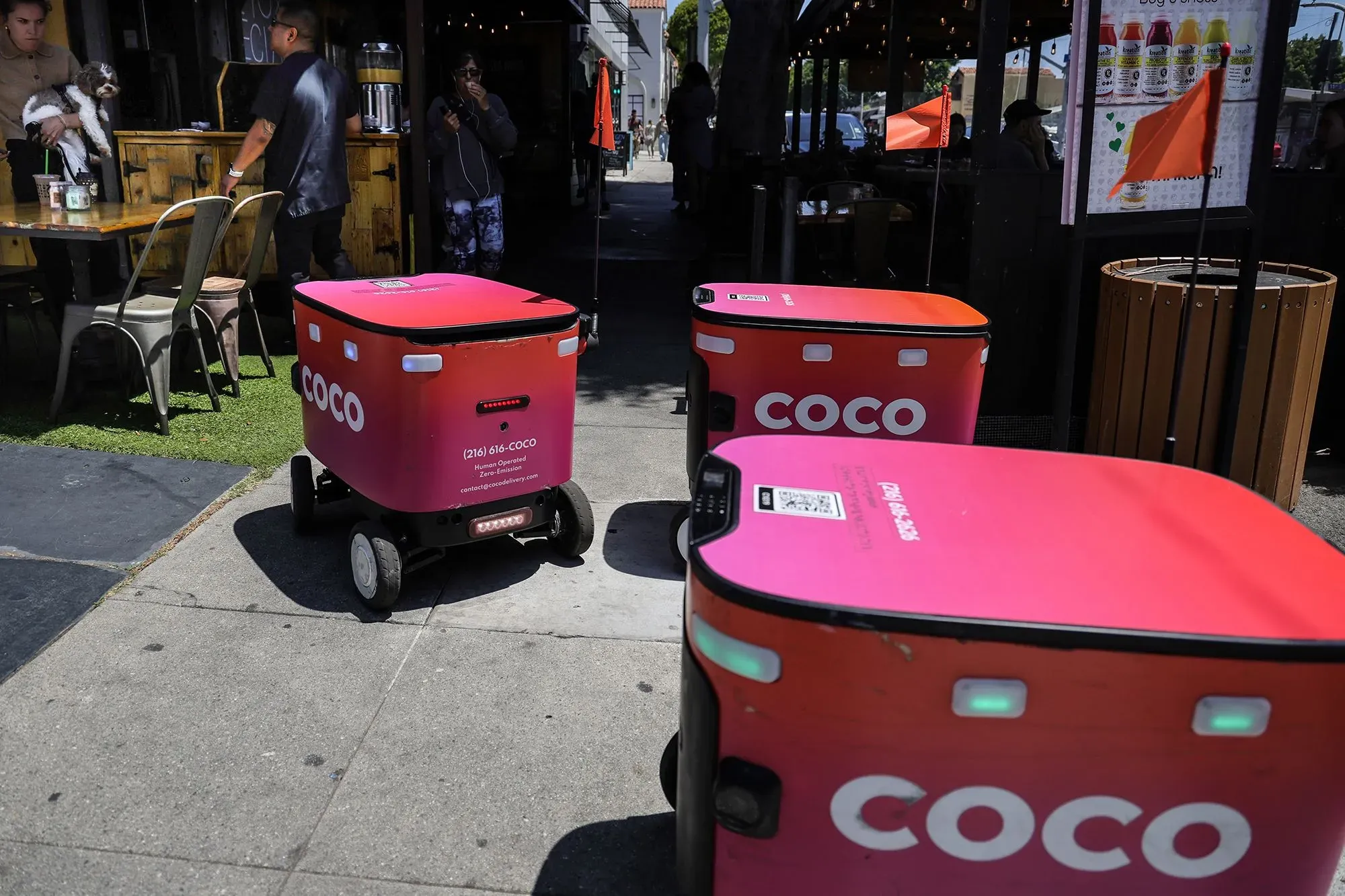 روبوتات توصيل الطعام "كوكو" بلون وردي، تتواجد أمام مطعم، تحمل طلبات الزبائن، تعكس تطور التكنولوجيا في خدمات التوصيل.
