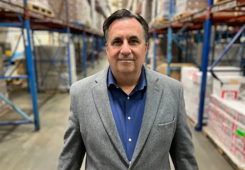 رجل يرتدي سترة رمادية يقف في مستودع مليء بالصناديق، يعبر عن القلق بشأن انعدام الأمن الغذائي المتزايد في الولايات المتحدة.