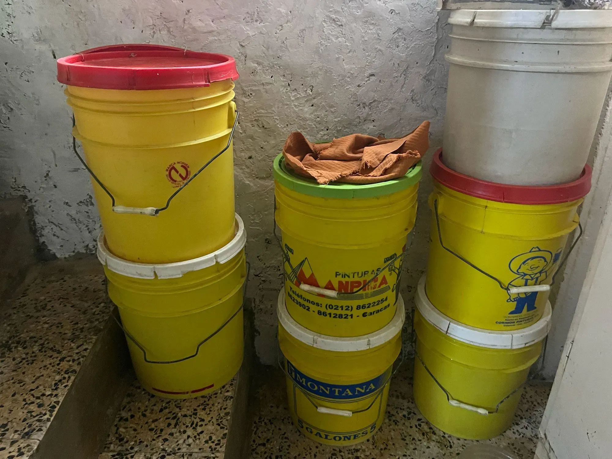 أوعية بلاستيكية ملونة تُستخدم لتخزين المياه، موضوعة بجانب الدرج، تعكس تحديات الحياة اليومية في فنزويلا بسبب نقص المياه.