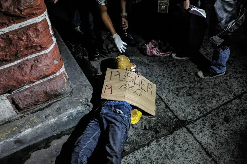 صورة لجثة شاب ممددة على الأرض، تحمل لافتة مكتوب عليها "مروج". تظهر تفاصيل عنف الحرب على المخدرات في الفلبين.