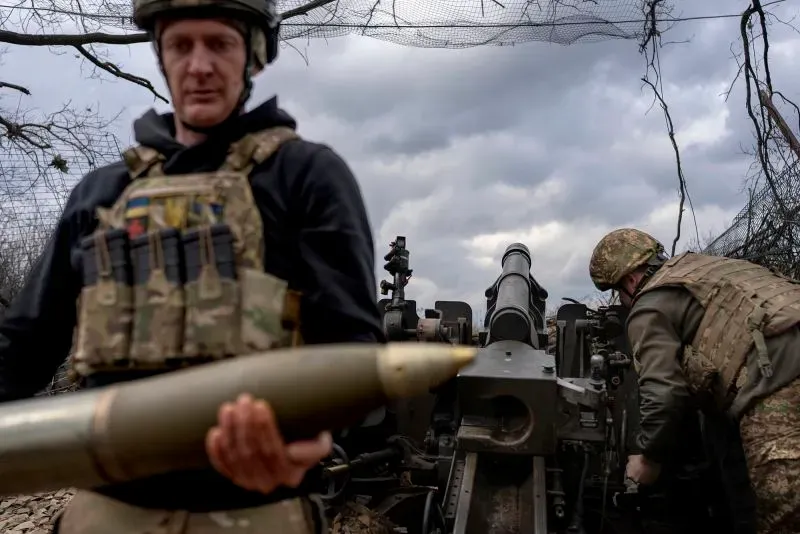 جنود أوكرانيون يستعدون لإطلاق قذيفة من مدفعية ثقيلة في ساحة المعركة، مع سماء غائمة تعكس أجواء الصراع المستمر في أوكرانيا.