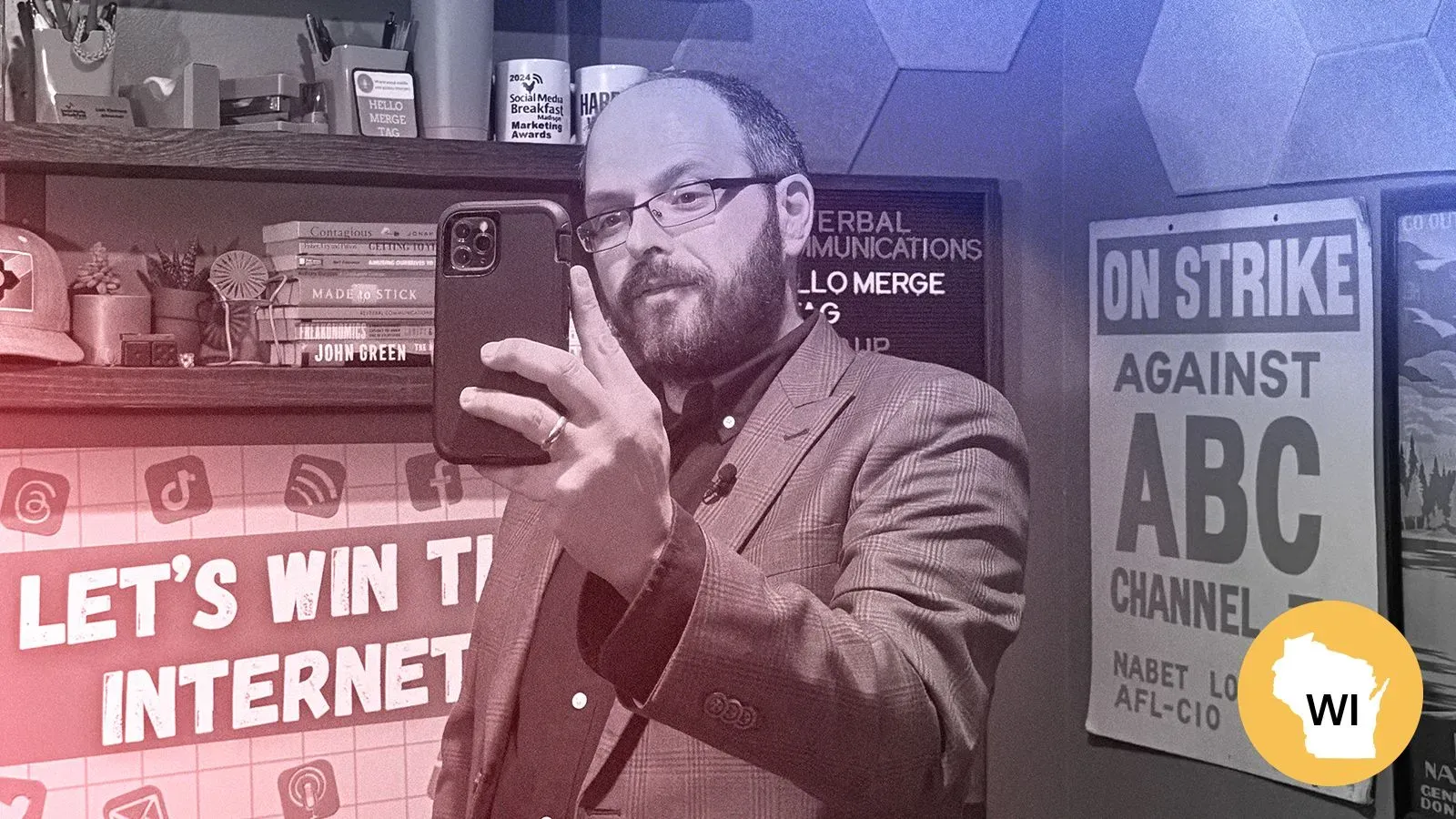 شخص يحمل هاتفه الذكي في استوديو، محاط بكتب وملصقات تتعلق بالانتخابات ووسائل التواصل الاجتماعي، يعبر عن أهمية التصويت.