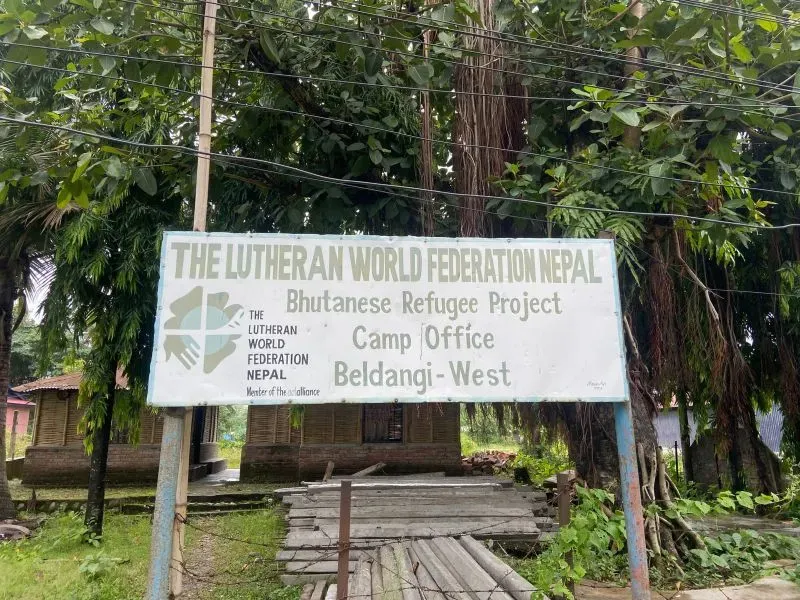 لافتة لمشروع اللاجئين البوتانيين في نيبال، تظهر اسم المعسكر وموقعه في بلدانغي غرب، محاطة بأشجار كثيفة.