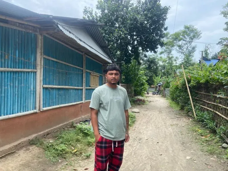شاب يقف في ممر ضيق بين المنازل، يعبر عن معاناته كلاجئ من بوتان بعد الترحيل إلى نيبال، حيث يعيش بدون وثائق.