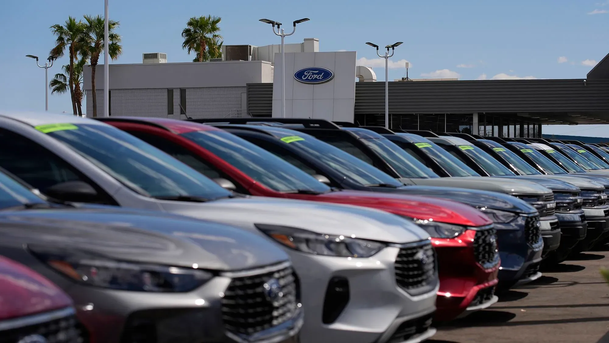 صف من السيارات الجديدة المتاحة للبيع في معرض فورد، مع وجود لافتات أسعار عليها، وخلفية المبنى المخصص لشركة فورد.