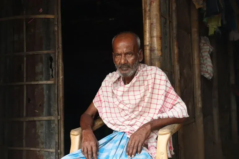 رجل مسن يجلس على كرسي خارج منزله في ولاية آسام، يعكس معاناته بعد اعتقاله وترحيله إلى بنغلاديش.