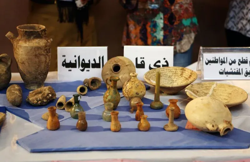 معرض يضم مجموعة من القطع الأثرية القديمة، بما في ذلك جرار وأوعية صغيرة، مع لافتات توضح مصدرها.