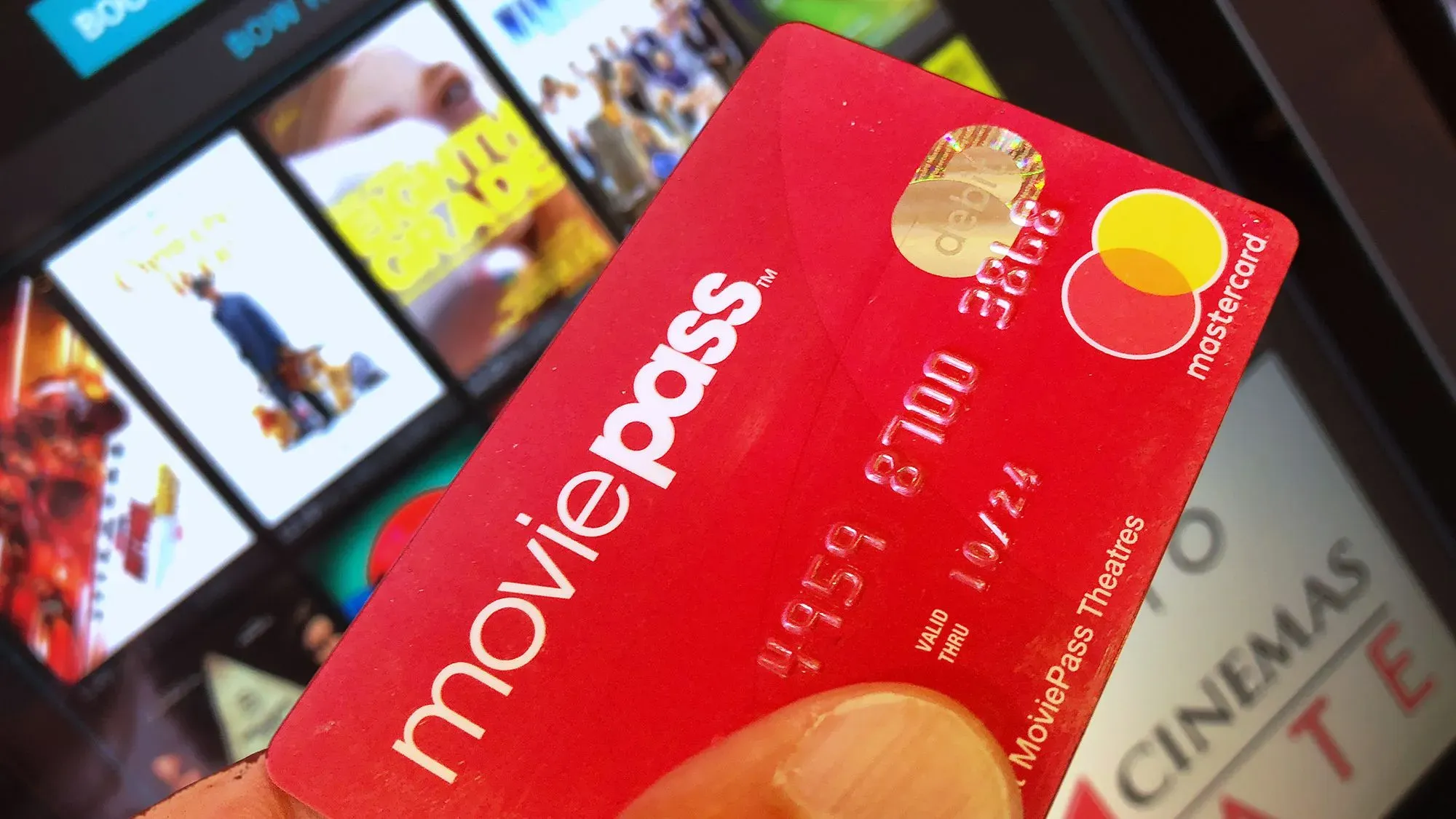 بطاقة MoviePass حمراء، تُظهر شعار الخدمة، مع خلفية تضم إعلانات أفلام، تعكس الجدل حول الاحتيال في الأوراق المالية.