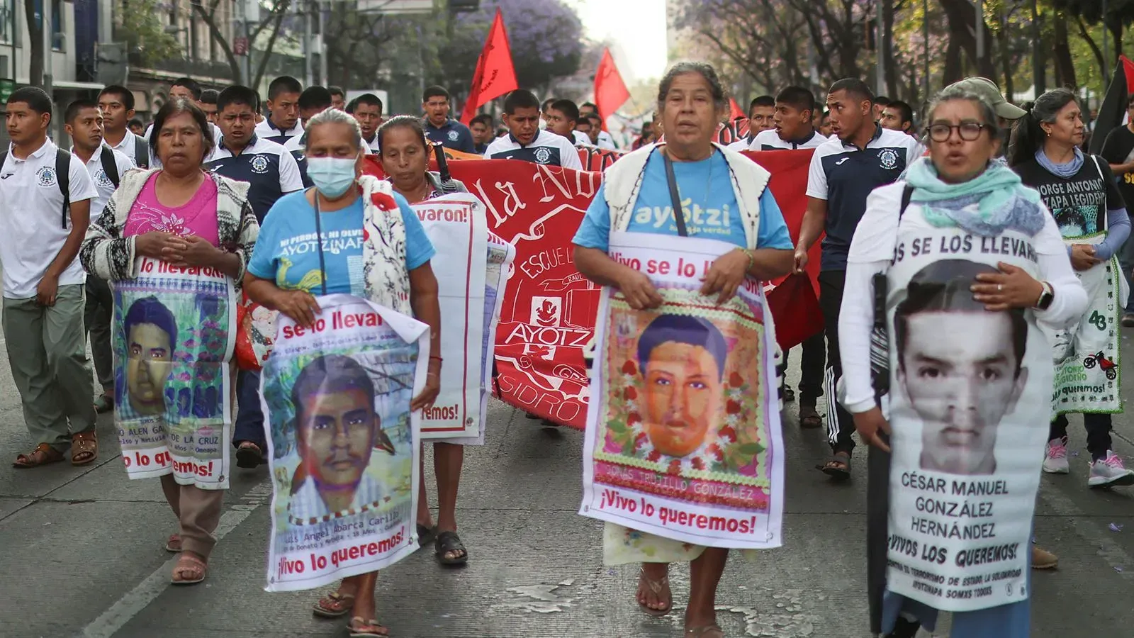 محتجون يسيرون في شوارع المكسيك يحملون لافتات وصورًا للطلاب المفقودين من كلية أيوتزينابا، مطالبين بالعدالة.