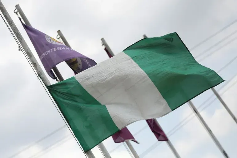 علم نيجيريا يرفرف في الهواء، مع أعلام أخرى في الخلفية، في سياق الاستعدادات لتكريم الرئيس السابق محمد بخاري.