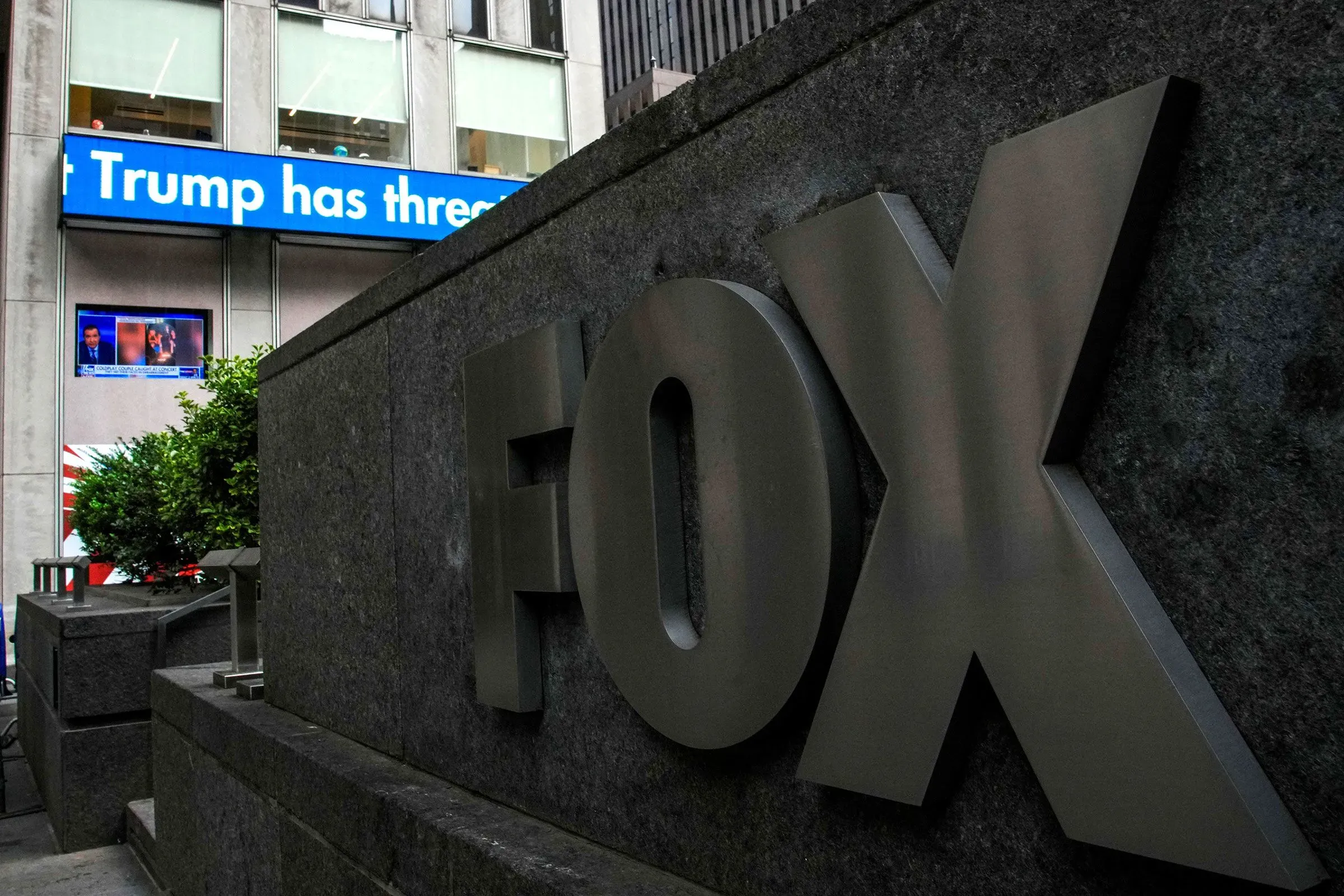 شعار قناة فوكس نيوز يظهر في المقدمة، مع شاشة تعرض أخبار تتعلق بالرئيس ترامب. تعكس الصورة التوترات حول حرية الصحافة والتعديل الأول.