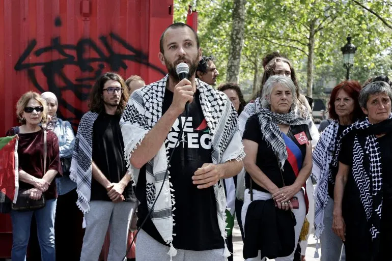 ناشط يتحدث إلى حشد في باريس، بينما يرتدي الكوفية، ويعبر عن دعم حقوق الفلسطينيين بعد اعتداءات أسطول غزة.
