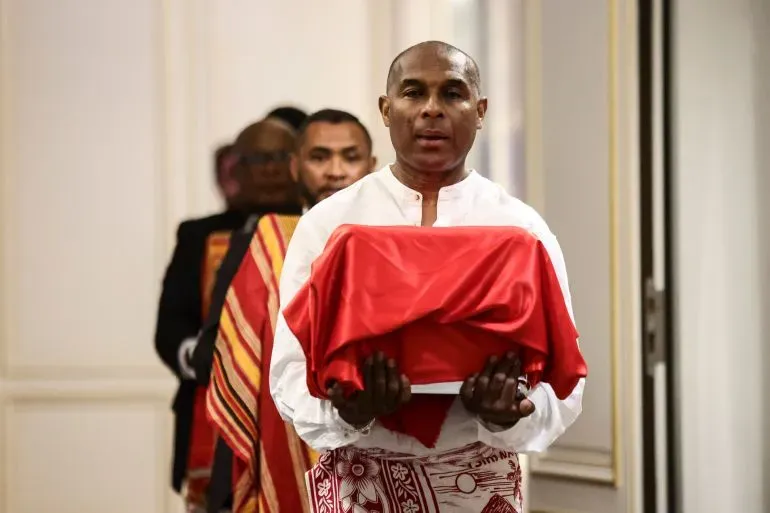 رجل يحمل صندوقًا مغطى بقماش أحمر خلال حفل تسليم جماجم بشرية إلى مدغشقر، في حدث يرمز إلى استعادة الذاكرة الثقافية.