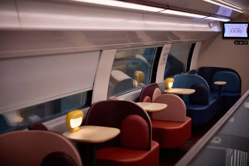 تصميم داخلي عصري لقطار INOUUI الفرنسي، يظهر مقاعد ملونة ومصابيح دافئة، يعكس الراحة والابتكار في السفر بالسكك الحديدية.