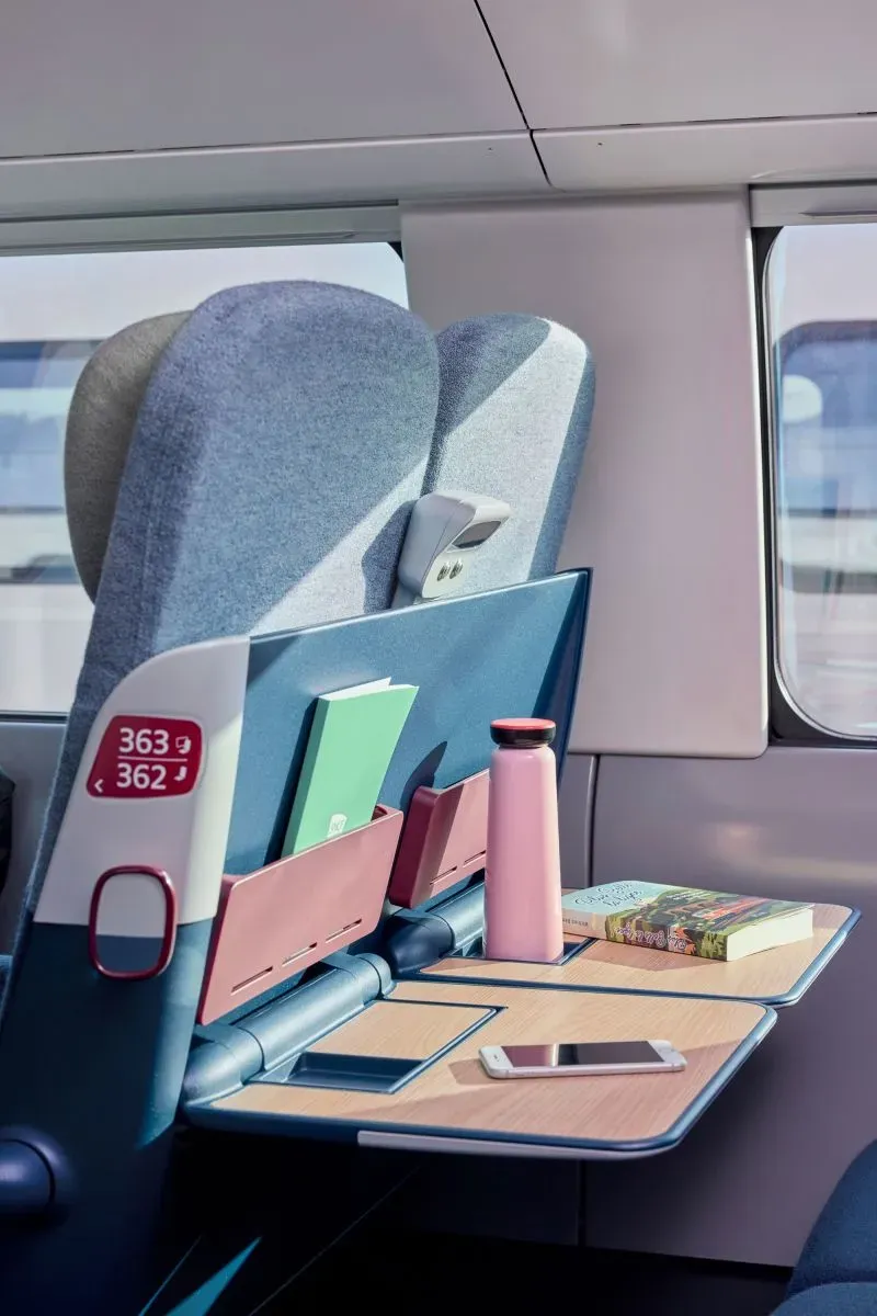 تصميم داخلي عصري لقطار INOUUI الجديد، يظهر مقعدًا مع طاولة قابلة للطي وحوامل للكتب وزجاجة مياه، يجسد الراحة والأناقة في السفر.