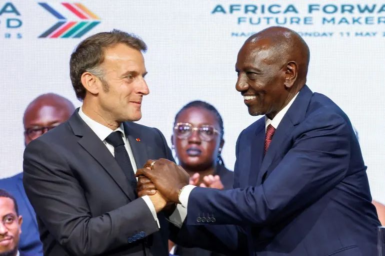 الرئيس الفرنسي إيمانويل ماكرون ورئيس كينيا ويليام روتو يتصافحان خلال قمة "Africa Forward" في نيروبي، مع خلفية تضم قادة أفارقة.